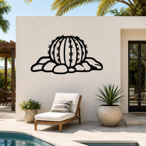Black metal barrel cactus wall art with spines and rocks cutout, mounted on a white outdoor wall beside a pool and lounge chair.