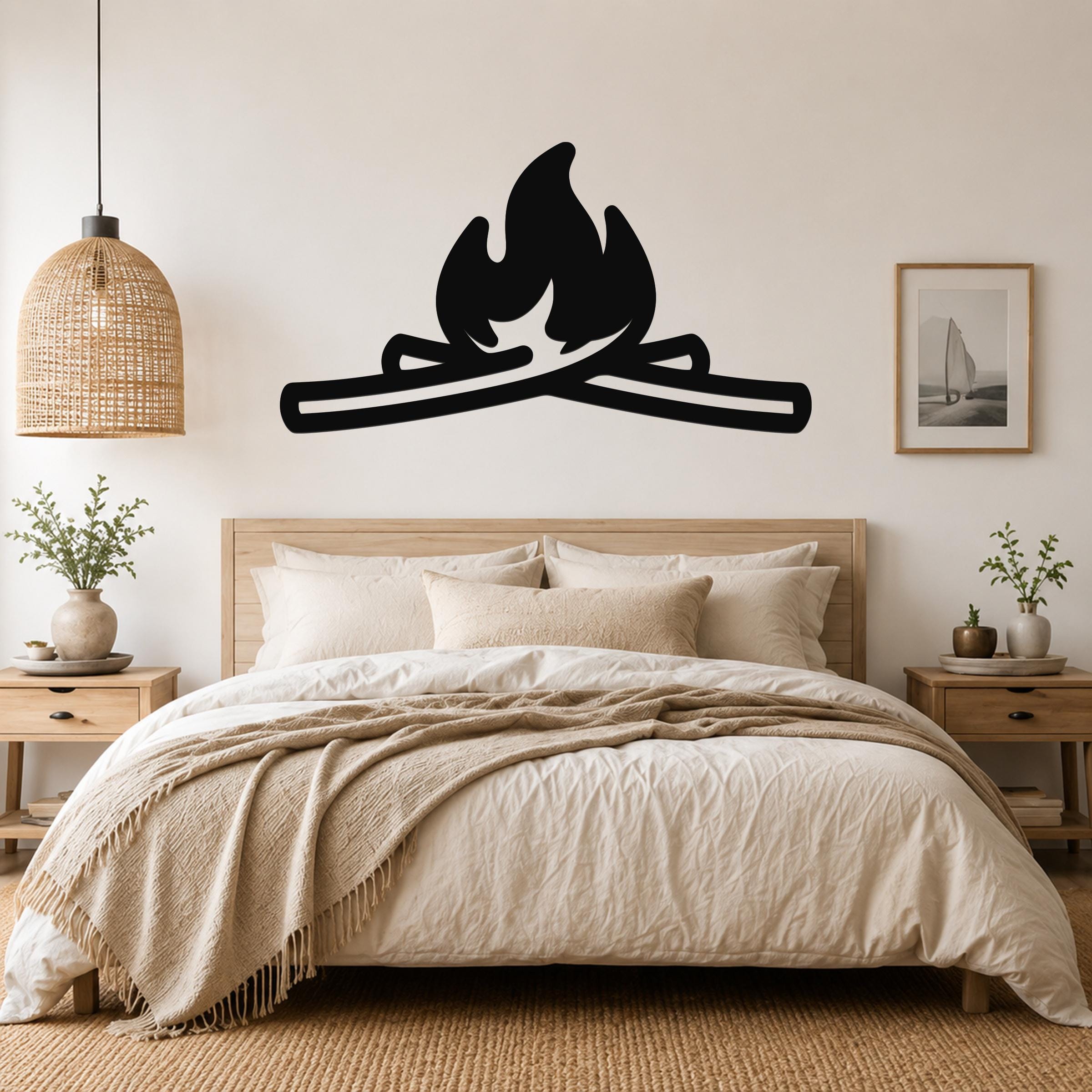 Black metal campfire wall art with flame and log silhouette, mounted above a wooden bed in a neutral bedroom.
