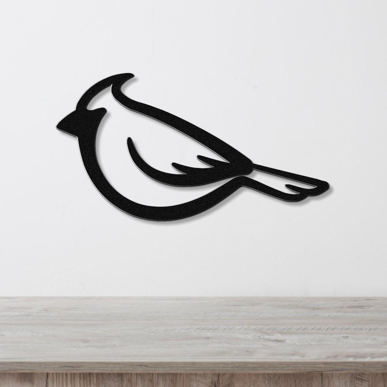Black metal cardinal wall art with a bold silhouette design, mounted on a white wall above a light wood surface.