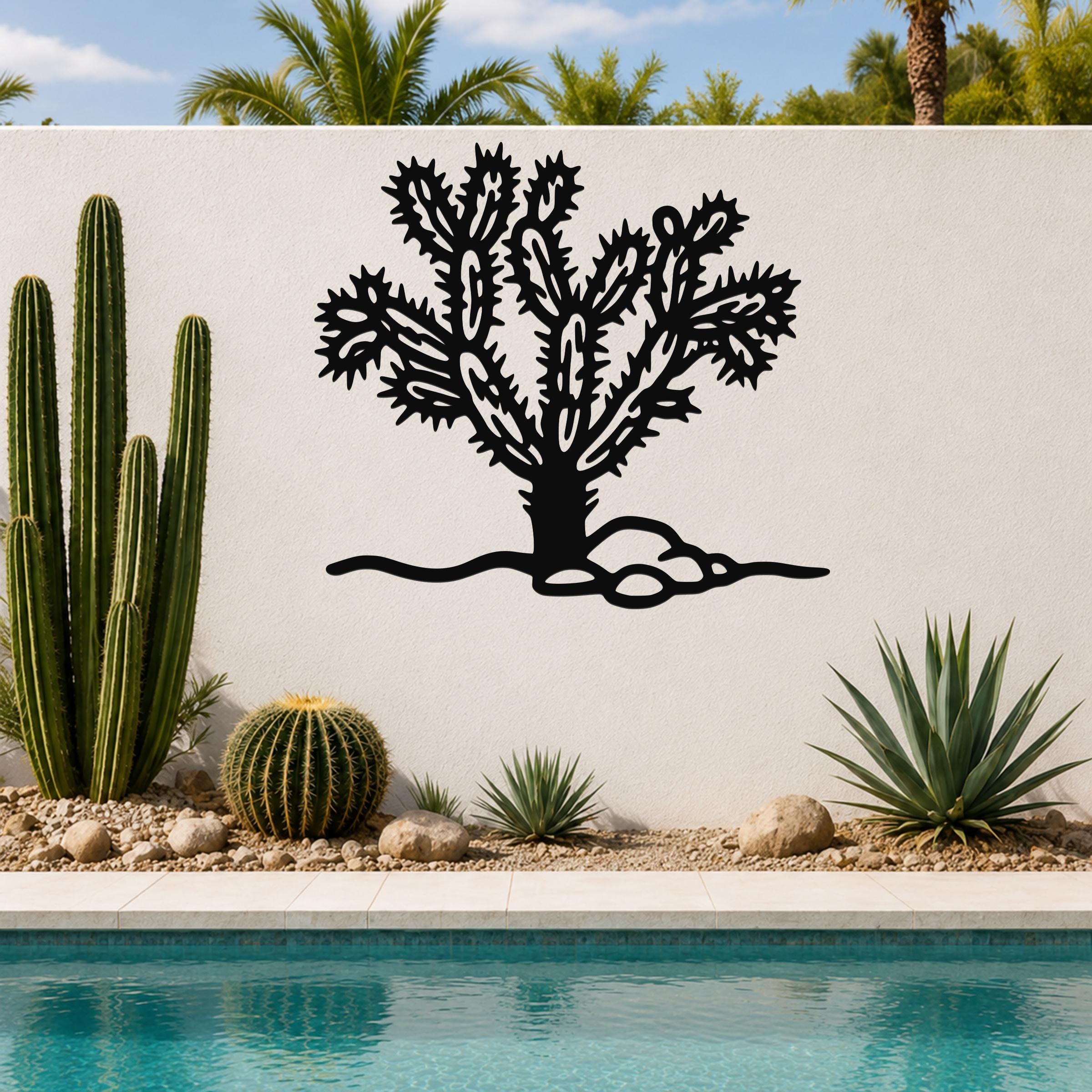 Black metal Cholla cactus wall art with intricate branch cutouts, mounted on a white outdoor wall above a poolside garden.