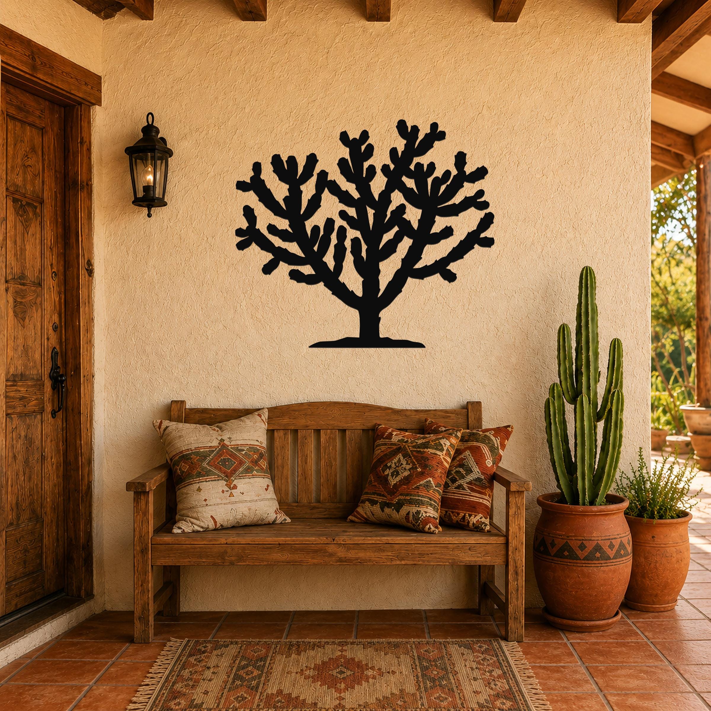Black metal Cholla cactus wall art silhouette mounted on a stucco wall above a wooden bench in a rustic patio entryway.