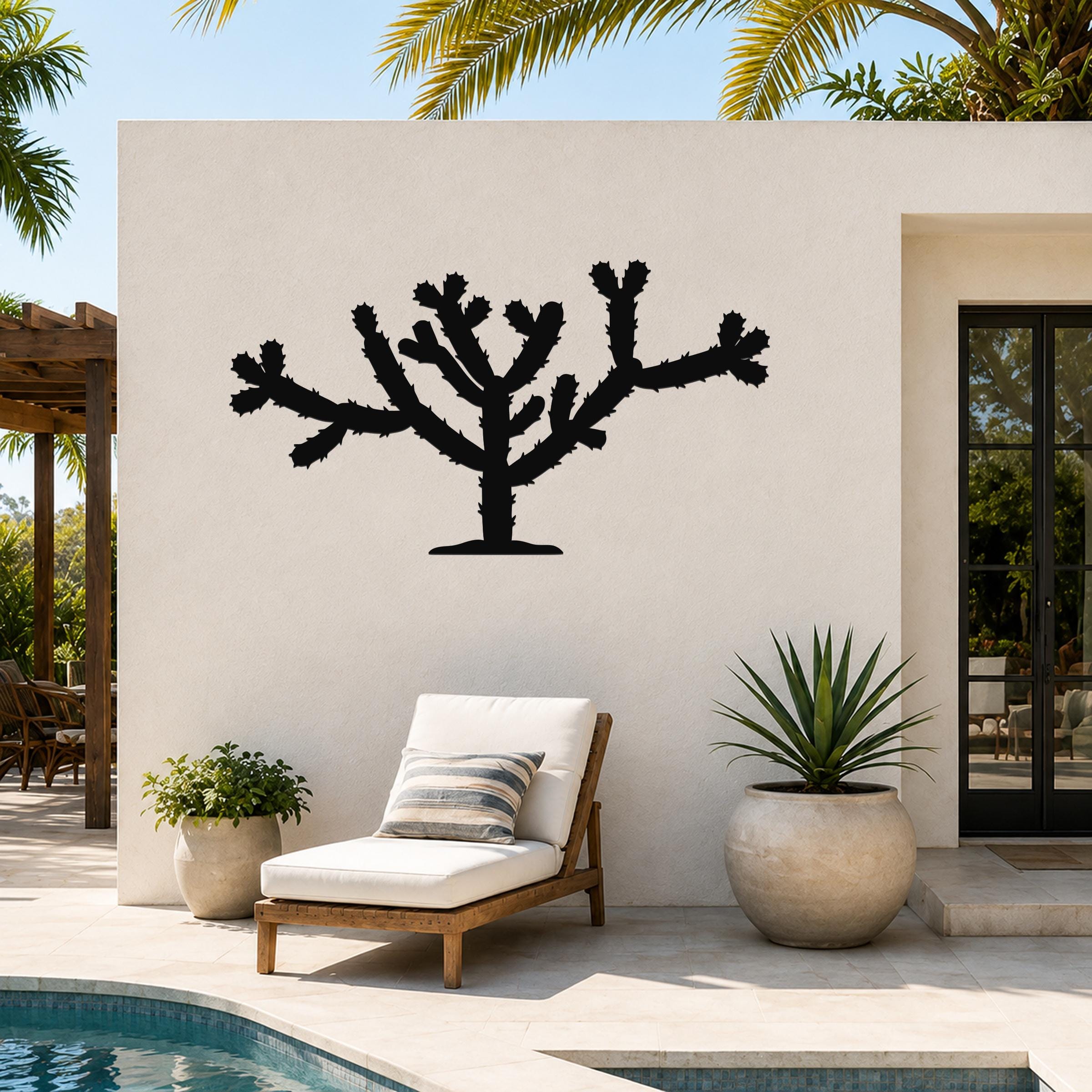 Black metal Cholla cactus wall art silhouette with branching arms and spines, mounted on a white outdoor wall beside a pool and lounge chair.