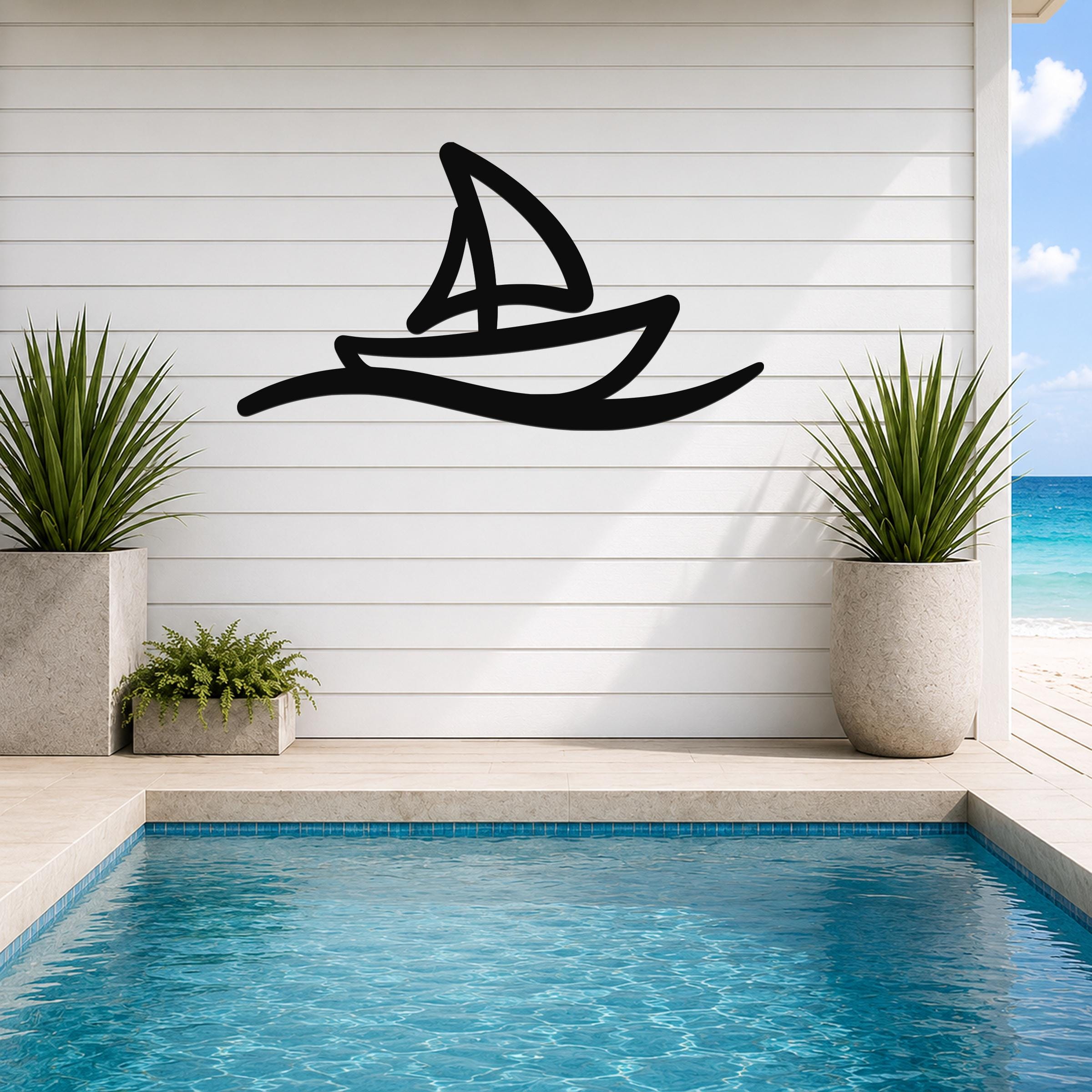 Black metal wall art in a sailboat silhouette with wave motion lines, mounted on a white shiplap wall above a pool in a coastal outdoor space.