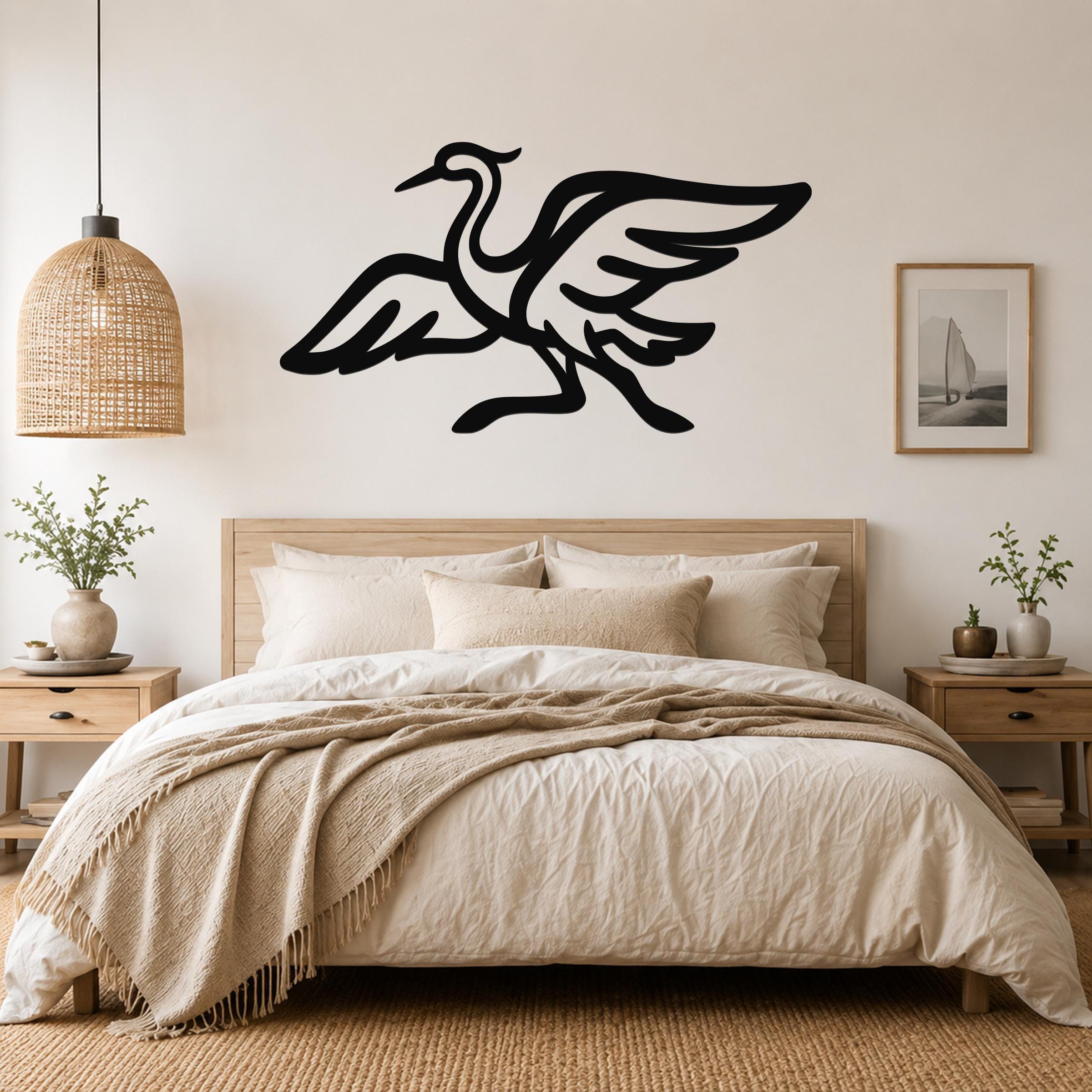 Black metal crane wall art with flowing wing and body cutouts, mounted above a wooden bed in a neutral bedroom.