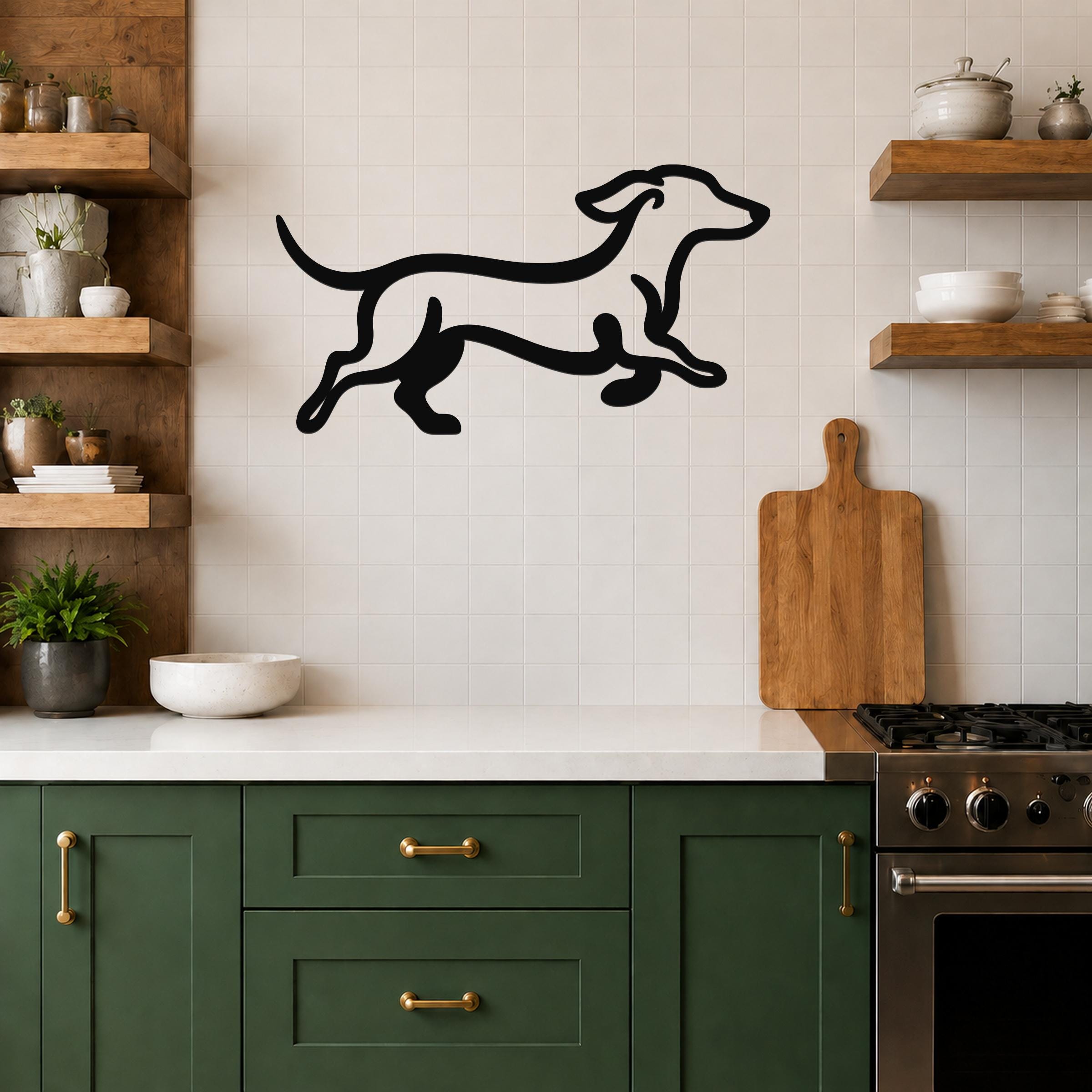 Black metal dachshund wall art in a running silhouette, mounted on a tiled kitchen wall above a counter with green cabinets and wooden shelves.
