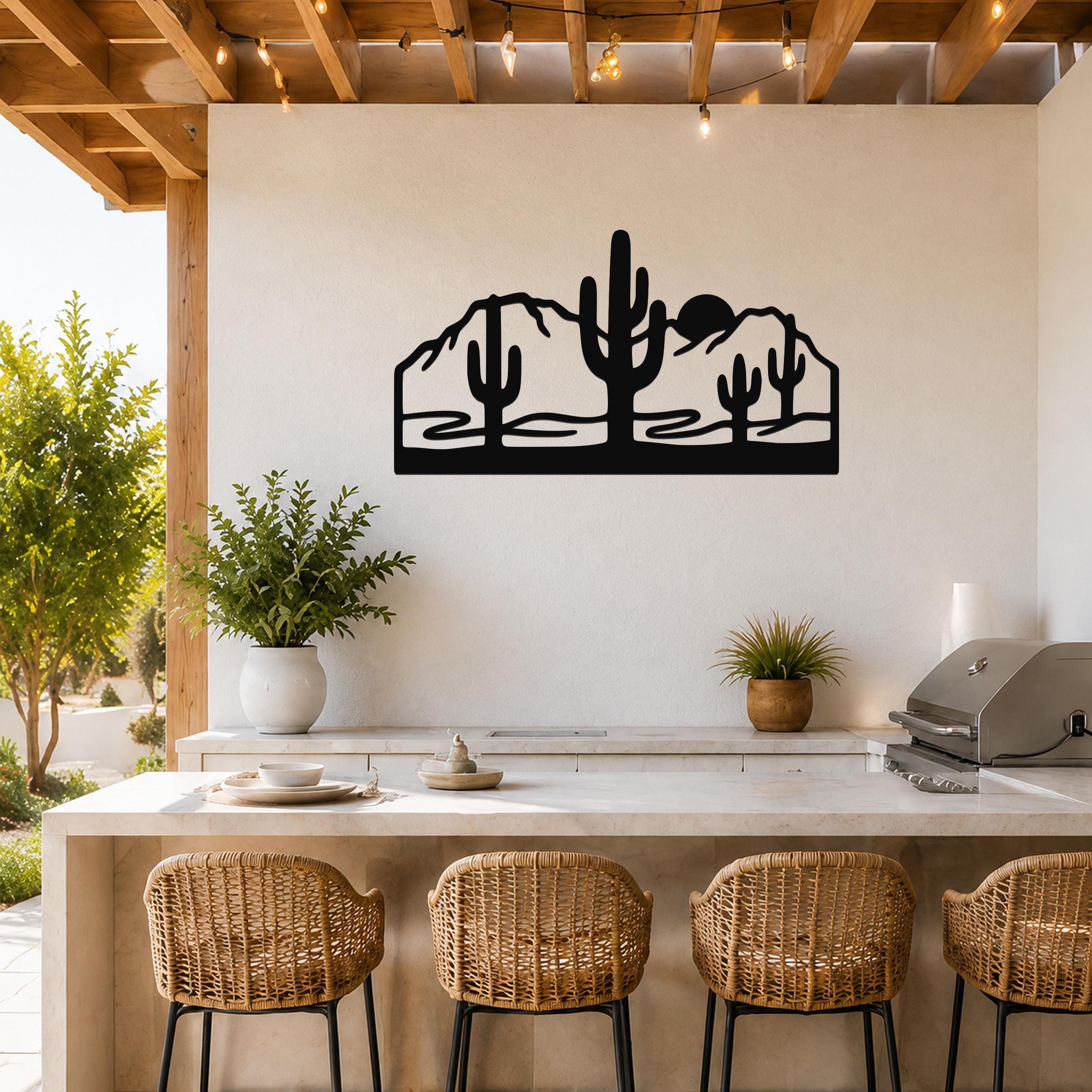 Black metal wall art with a desert silhouette of saguaro cacti and mountains, mounted on a white wall above a kitchen counter.