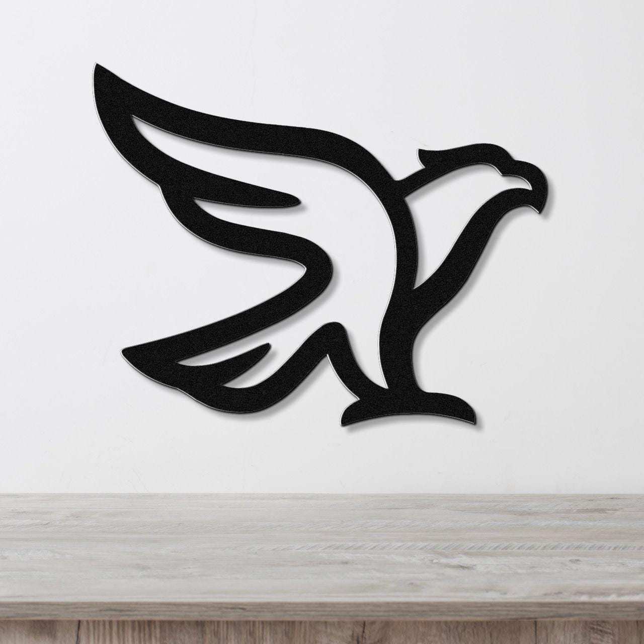 Black metal eagle wall art with a bold silhouette design, mounted on a white wall above a light wood surface.