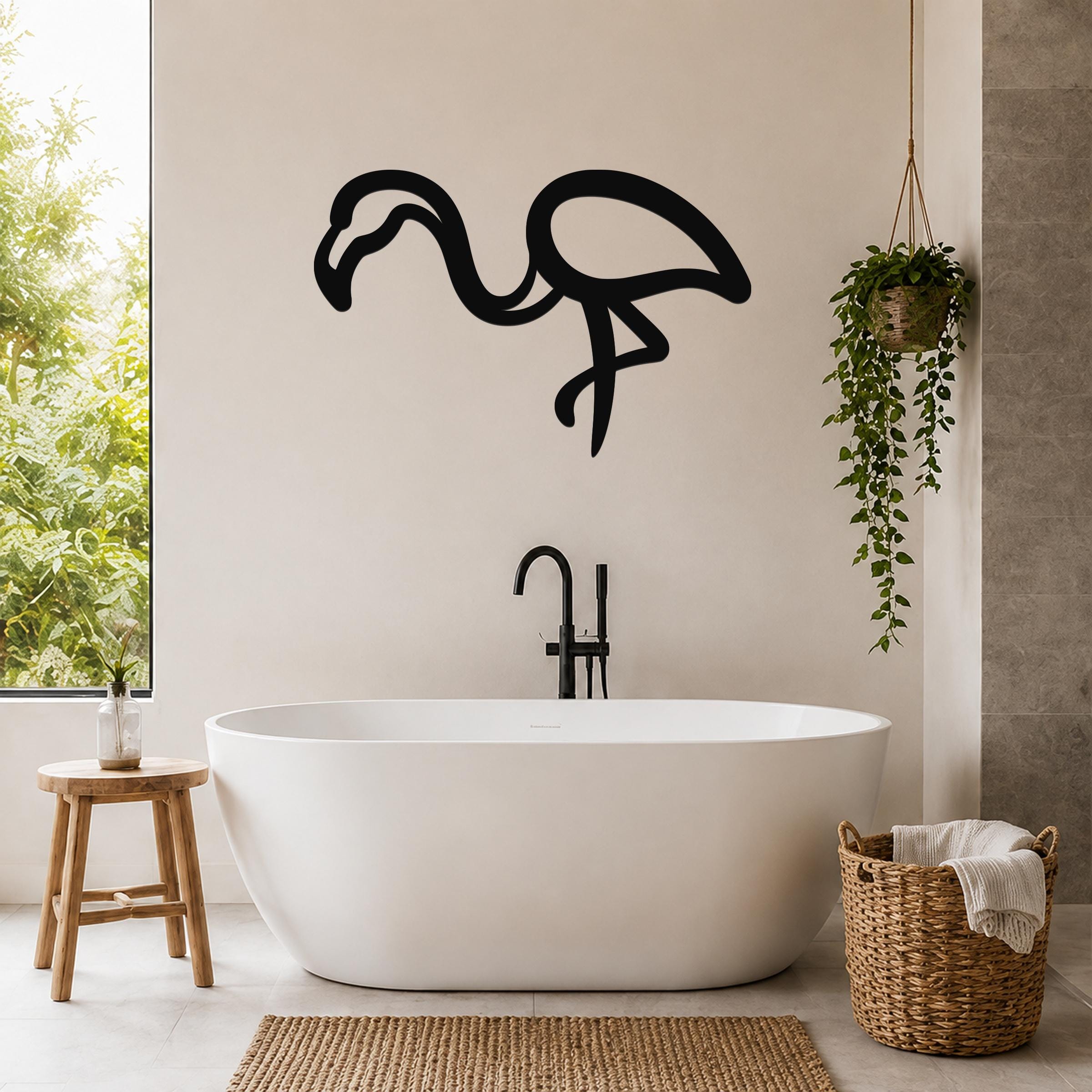 Black metal flamingo wall art silhouette mounted on a bathroom wall above a freestanding tub, with a hanging plant and woven basket nearby.