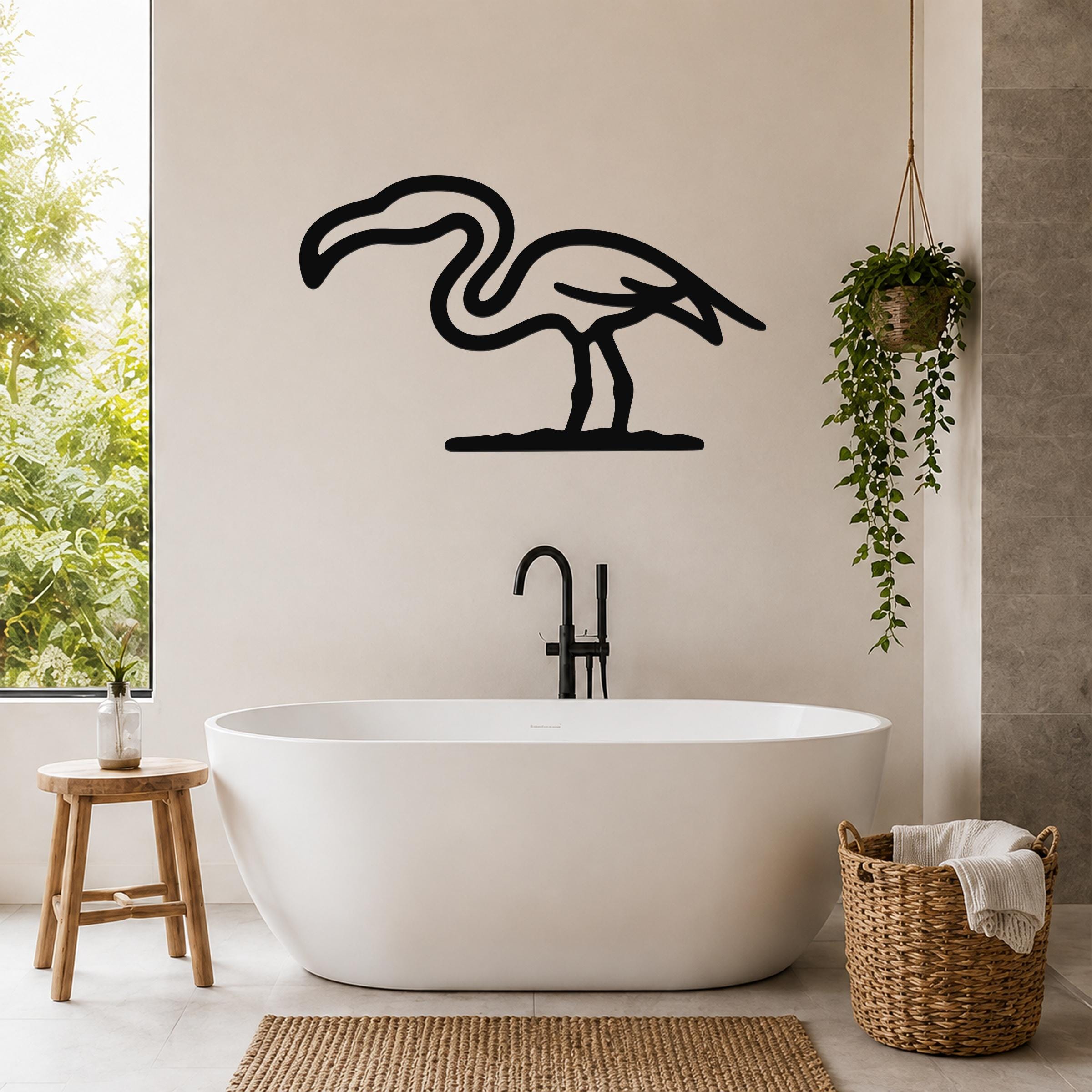 Black metal flamingo wall art silhouette mounted on a bathroom wall above a freestanding tub, with a hanging plant and woven basket nearby.