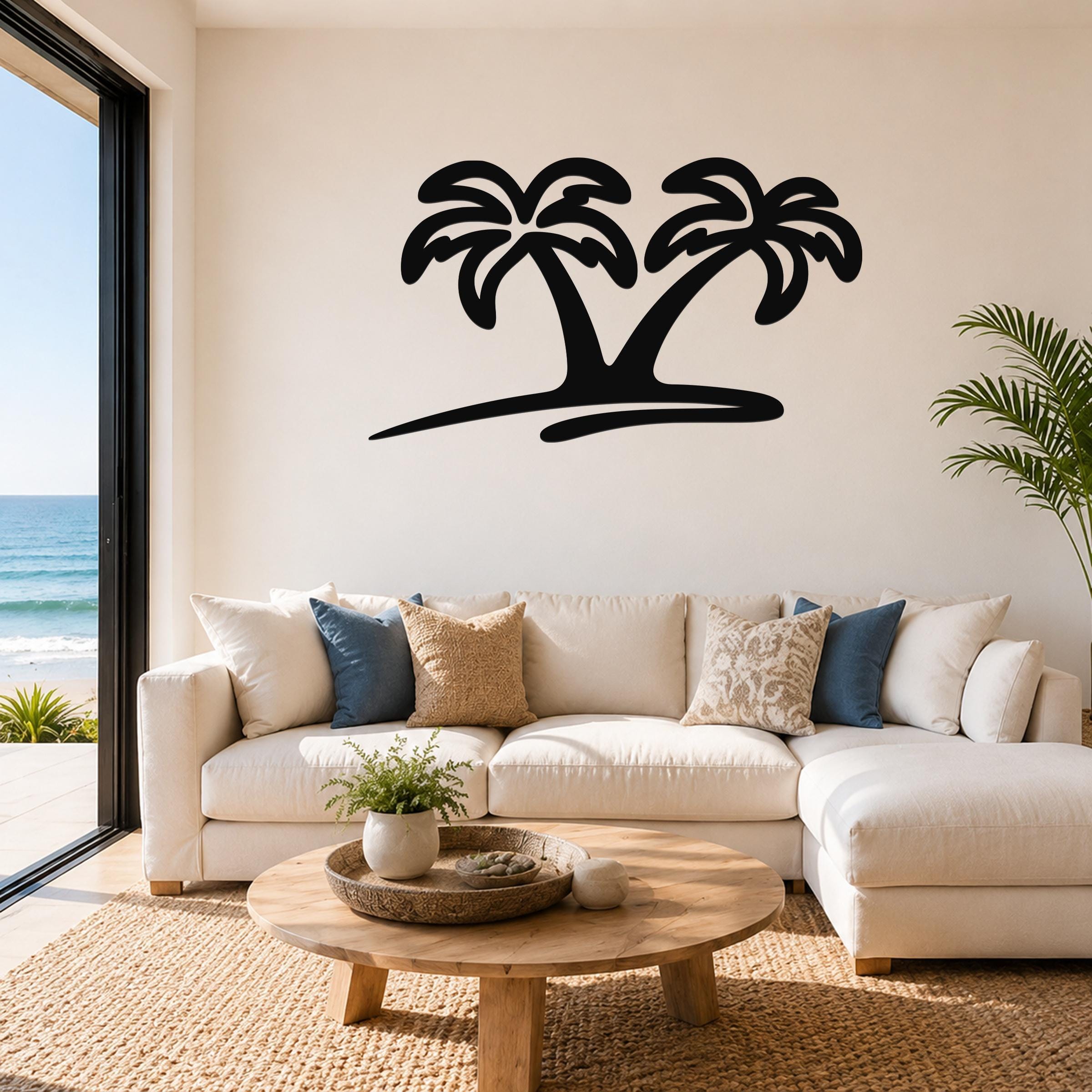 Black metal palm tree wall art with two silhouetted trees and a curved base, mounted above a white sofa in a living room with ocean views.