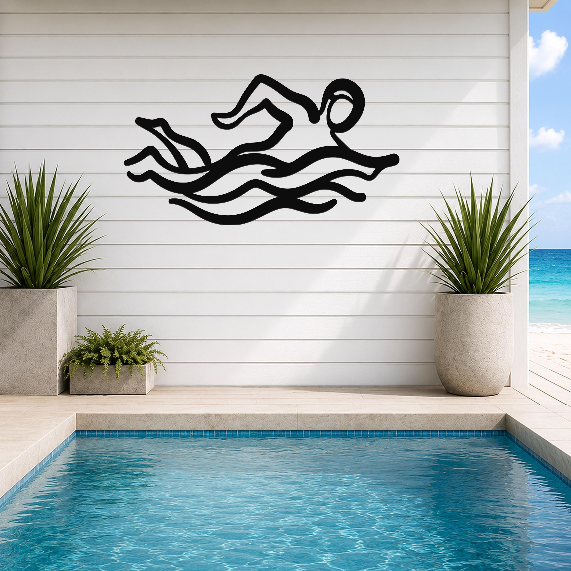 Black metal swimmer wall art with motion-line cutouts, mounted on a white shiplap wall above a pool in a patio setting.