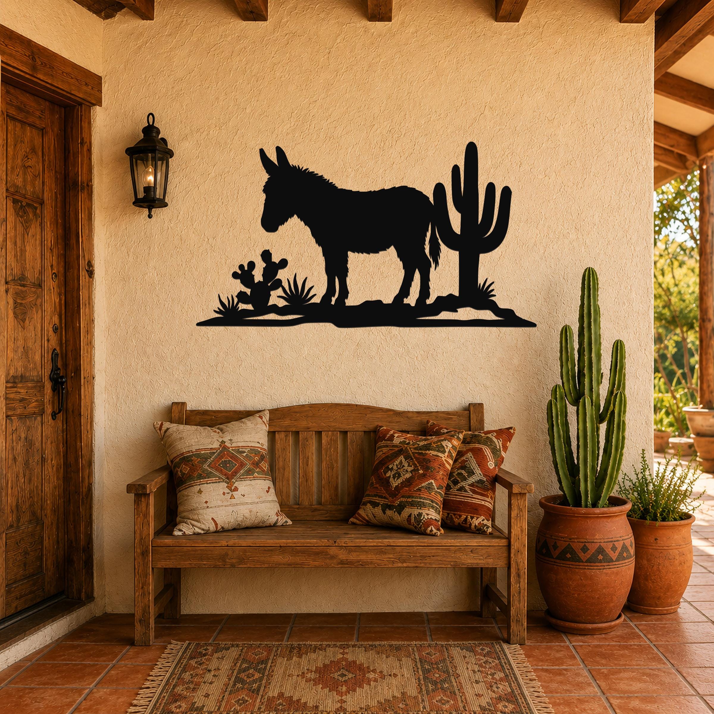 Black metal wall art silhouette of a burro and cacti, mounted on a stucco wall above a wooden bench in a rustic patio entry.