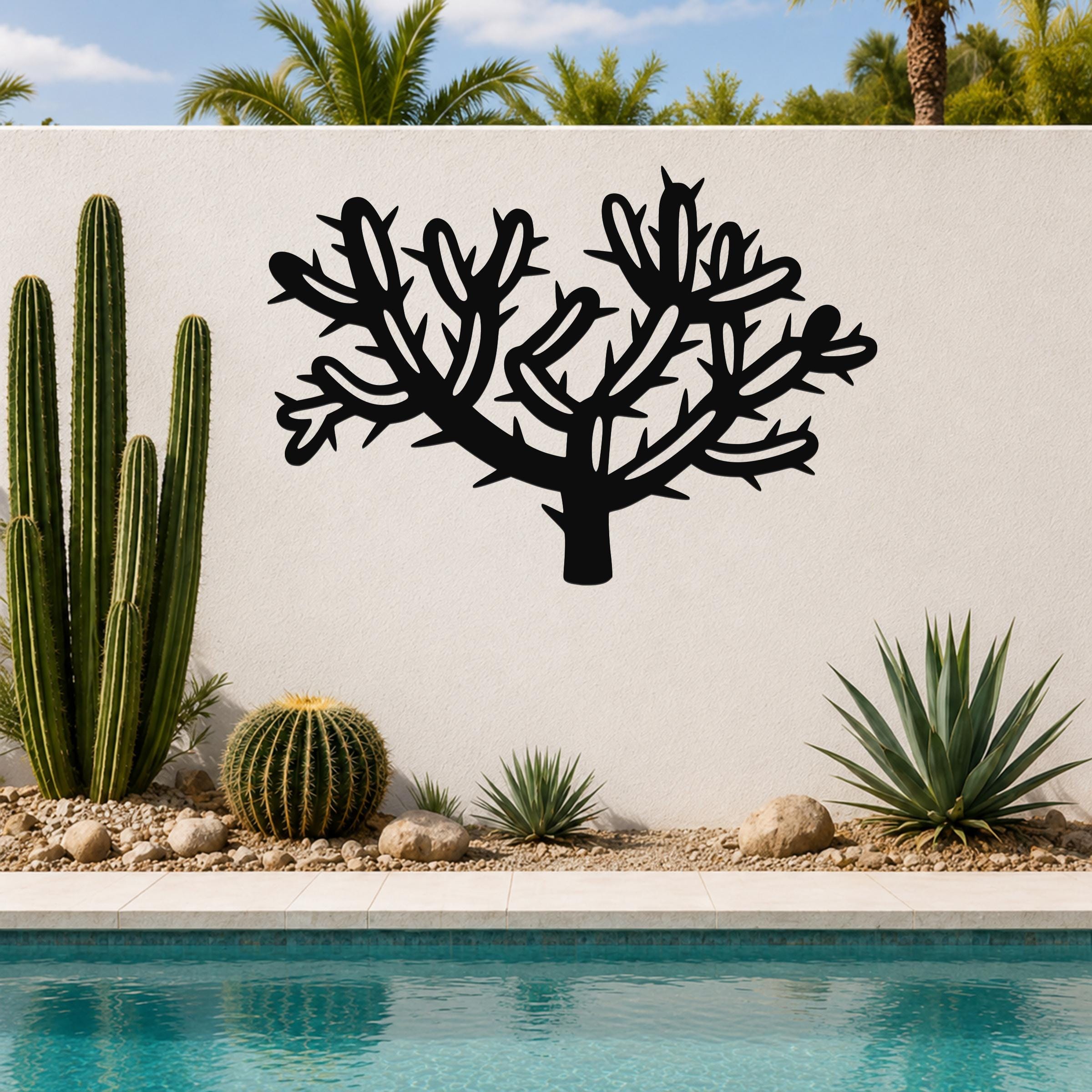 Black metal Cholla cactus wall art with branching spines and cutout details, mounted on a white outdoor wall beside a pool and desert plants.