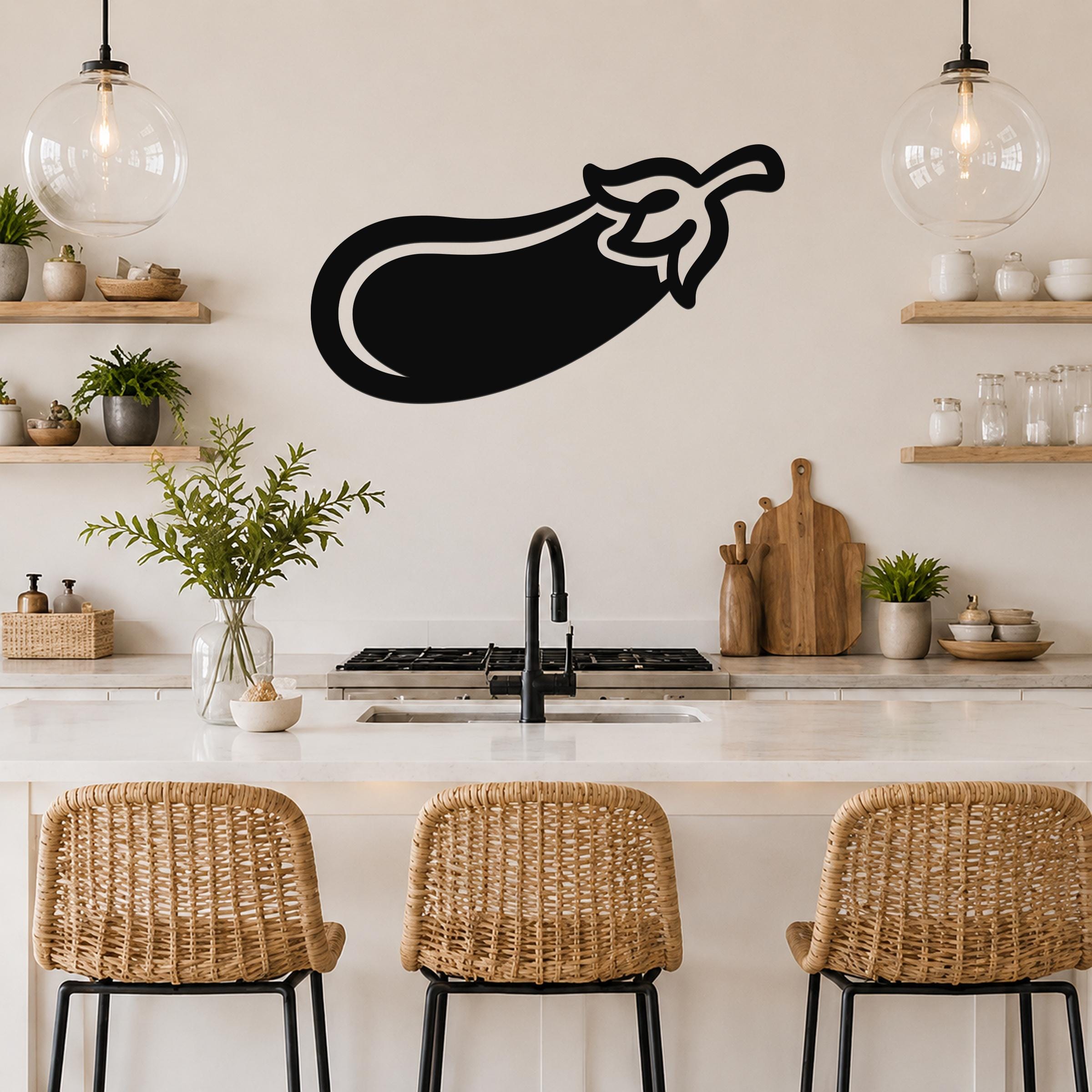 Black metal eggplant wall art with a bold silhouette design, mounted on a kitchen wall above a counter with wicker bar stools.