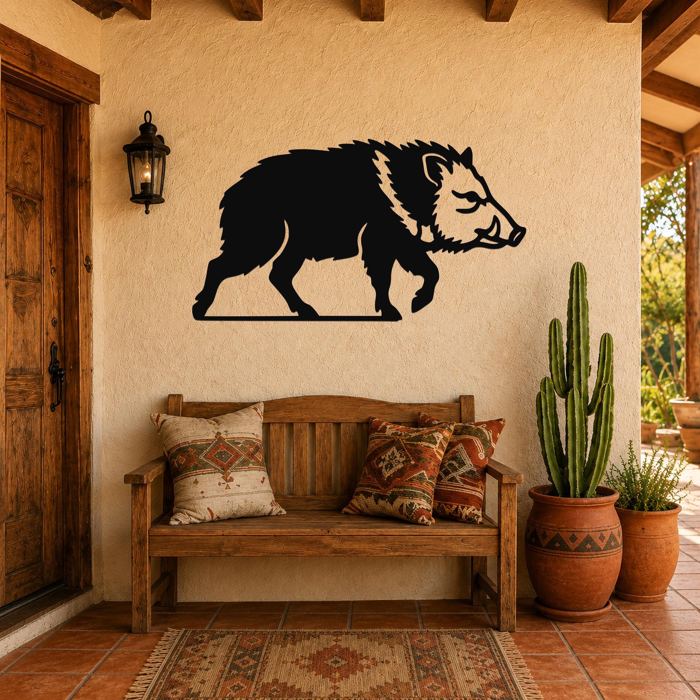 Black metal javelina wall art silhouette mounted on a stucco wall above a wooden bench in a covered patio entryway.