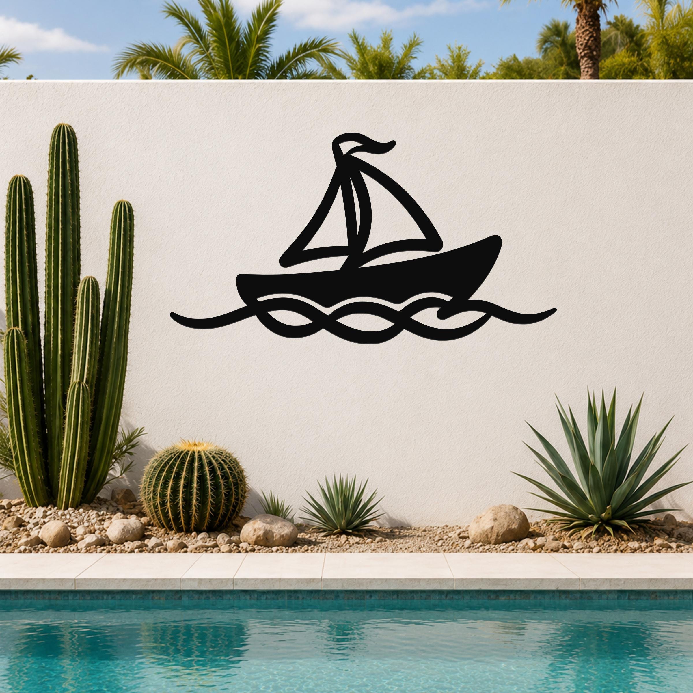 Black metal sailboat wall art with wave cutouts, mounted on a white outdoor wall above a pool with cacti and palm trees in the background.