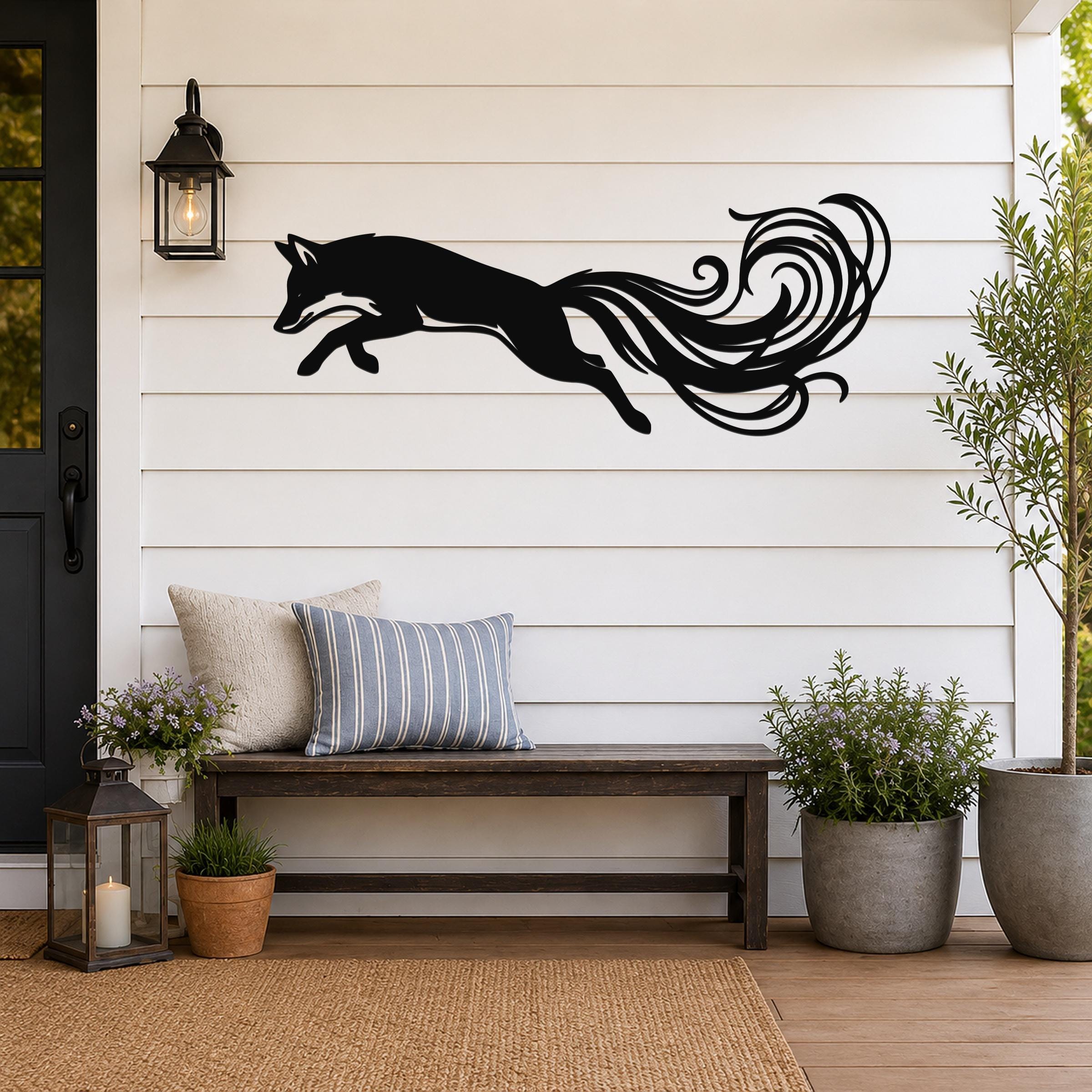 Black metal fox wall art with flowing tail cutouts, mounted on a white shiplap wall above a wooden bench on a porch.