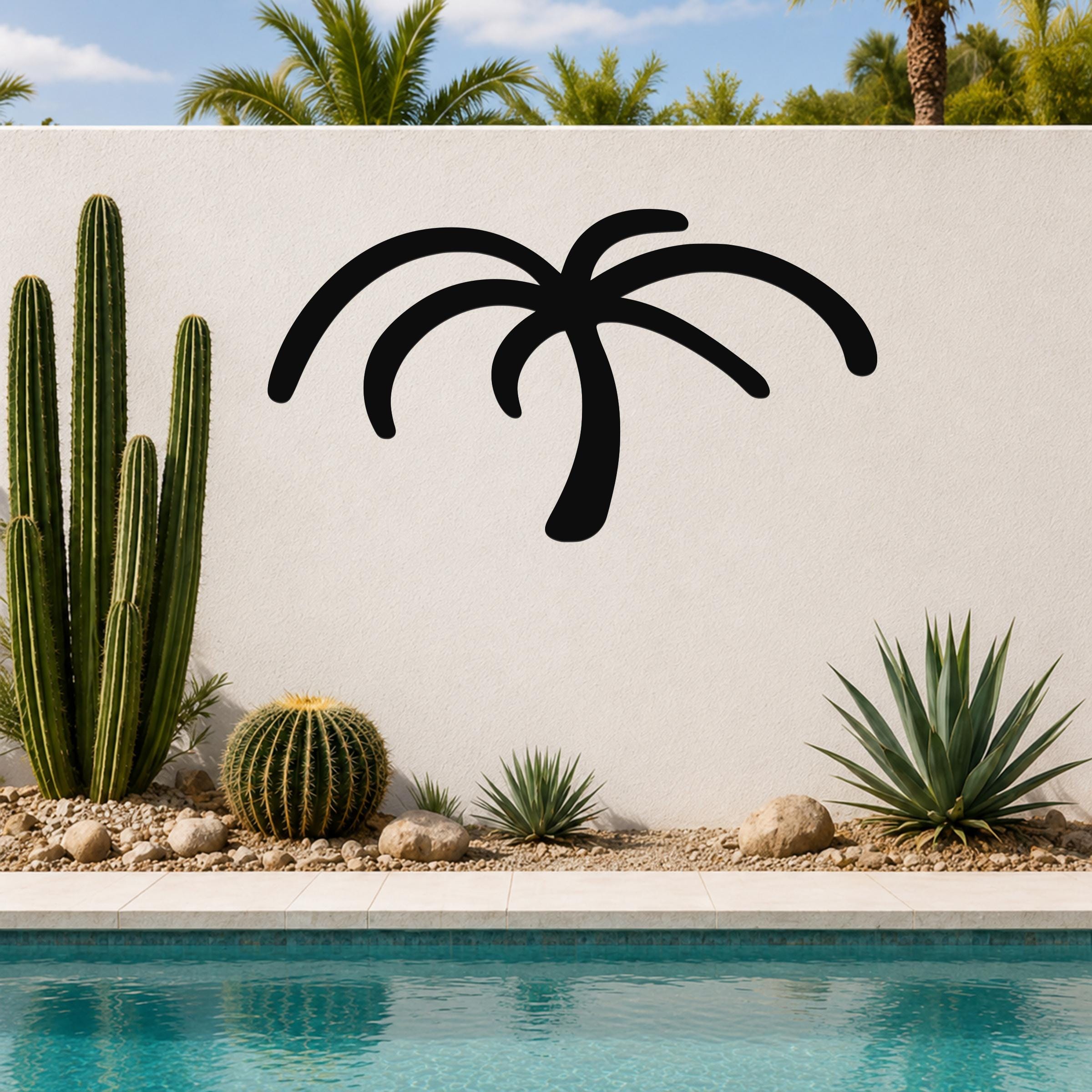 Black metal palm tree wall art with curved frond cutouts, mounted on a white outdoor wall above a pool with cacti and succulents.