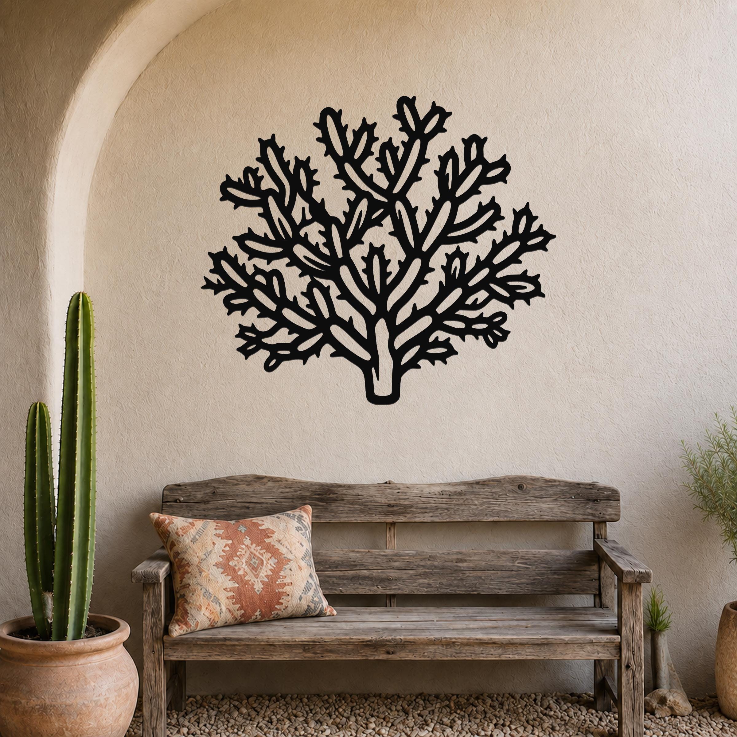 Black metal Cholla cactus wall art with intricate branch cutouts, mounted on a textured beige wall above a rustic wooden bench in a desert-themed entryway.