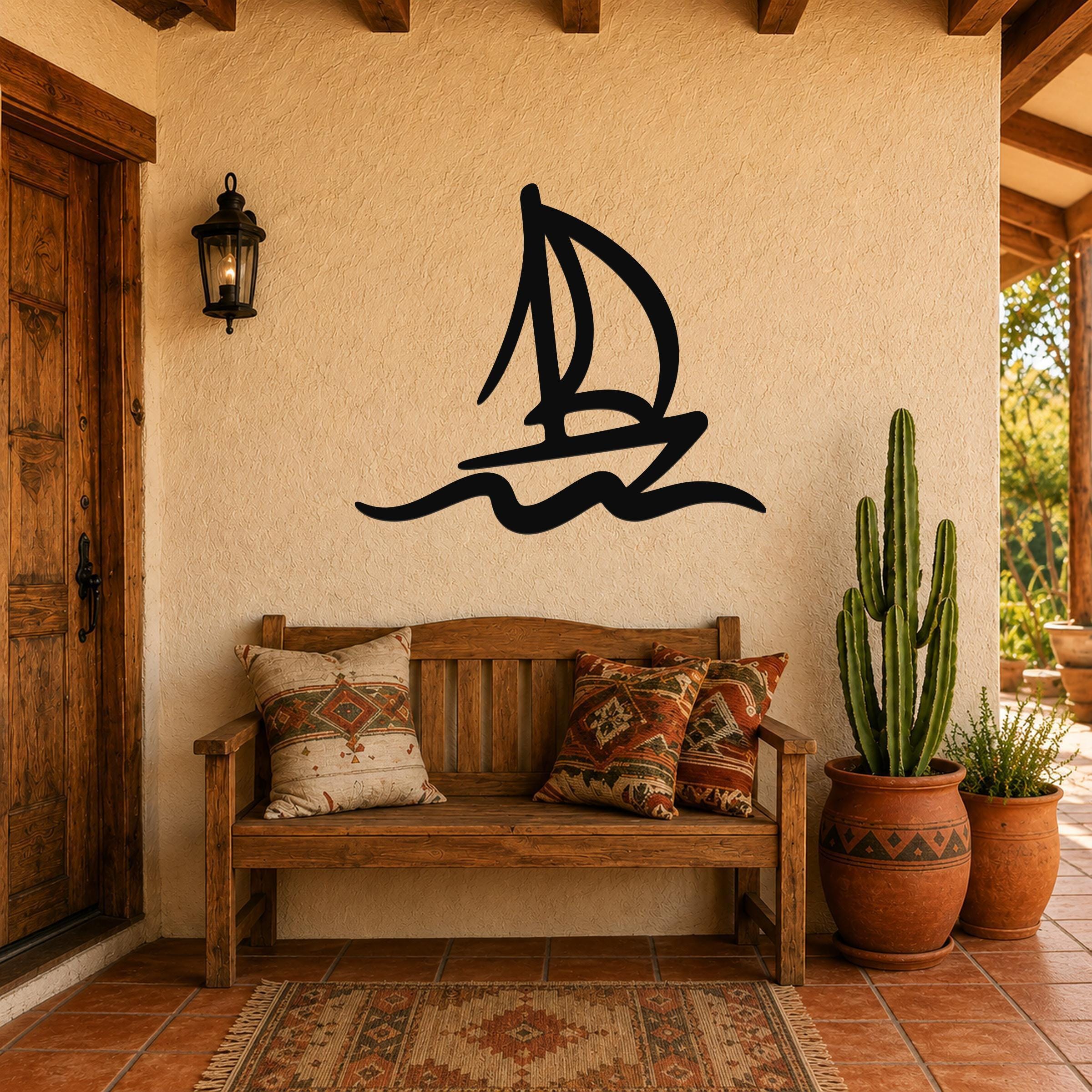 Black metal sailboat wall art with wave cutouts, mounted on a stucco wall above a wooden bench in a rustic patio entryway.