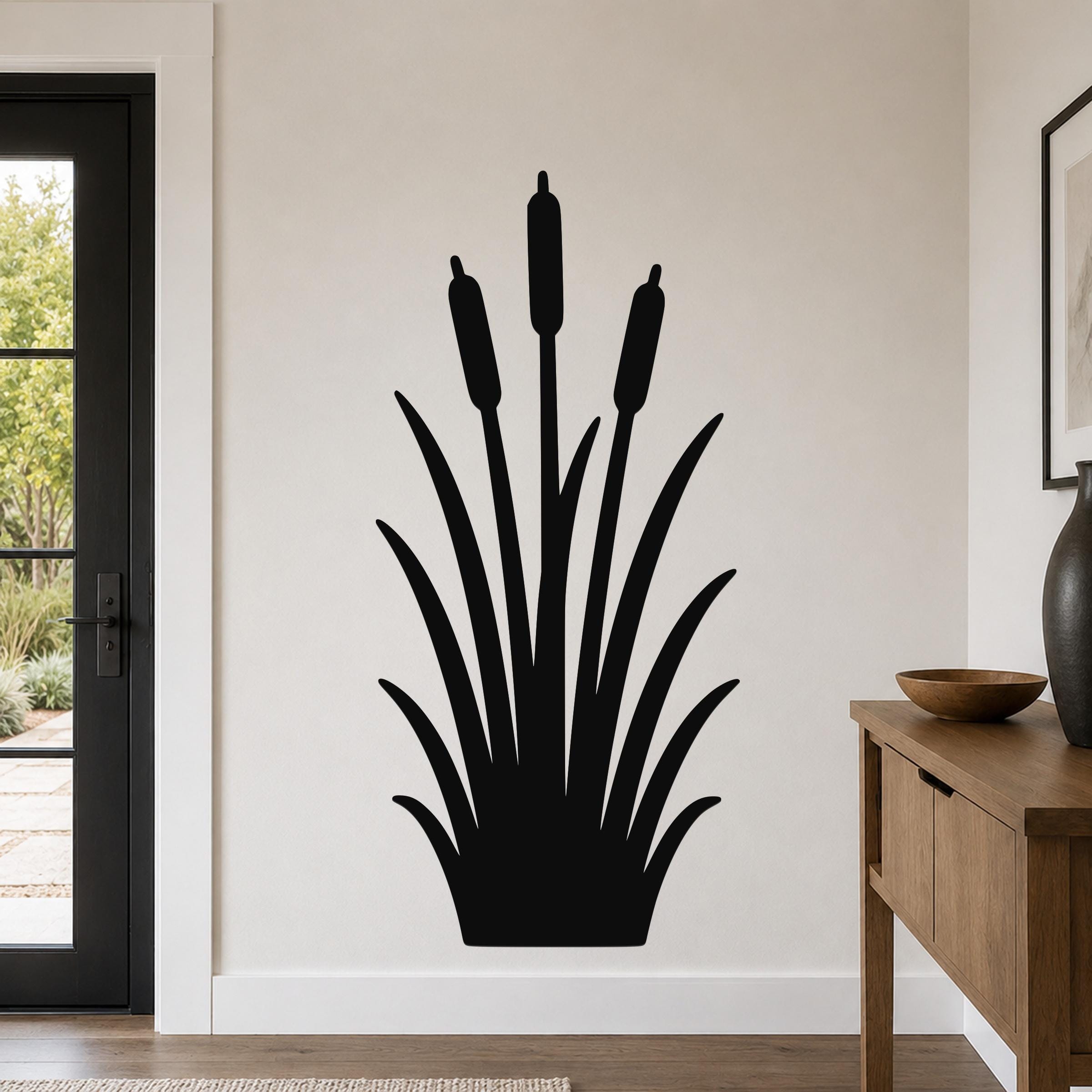 Black metal cattail wall art with a silhouette design of tall reeds and seed heads, mounted on a living room wall above a wooden console table.
