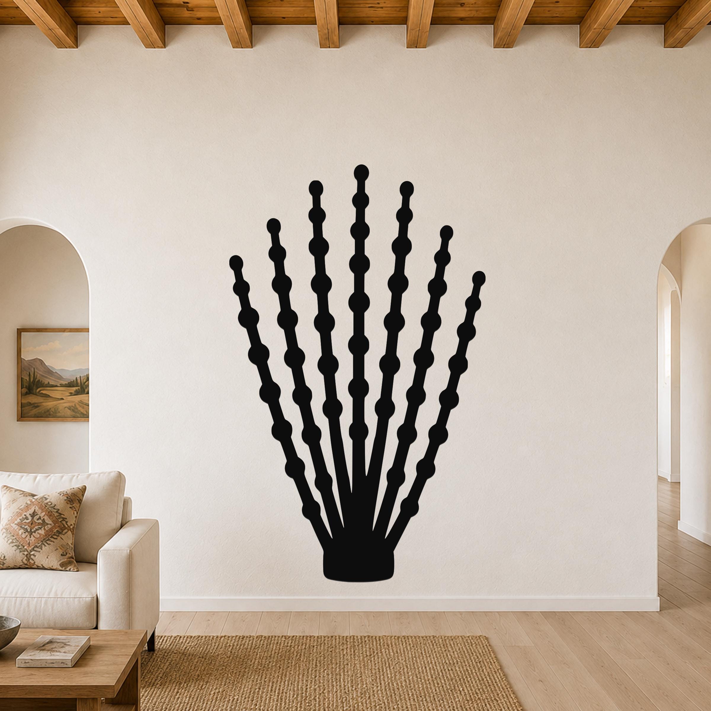 Black metal ocotillo wall art with branching stem and bead-like cutouts, mounted on a living room wall above a sofa.