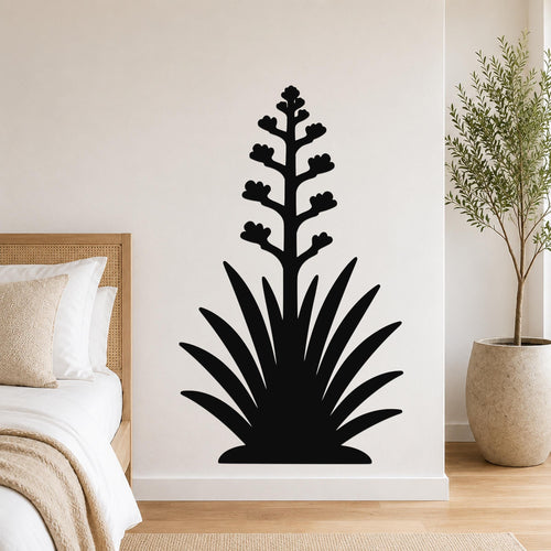 Black metal wall art silhouette of a blooming agave plant with spiky leaves and flower stalk, mounted on a bedroom wall above a bed.