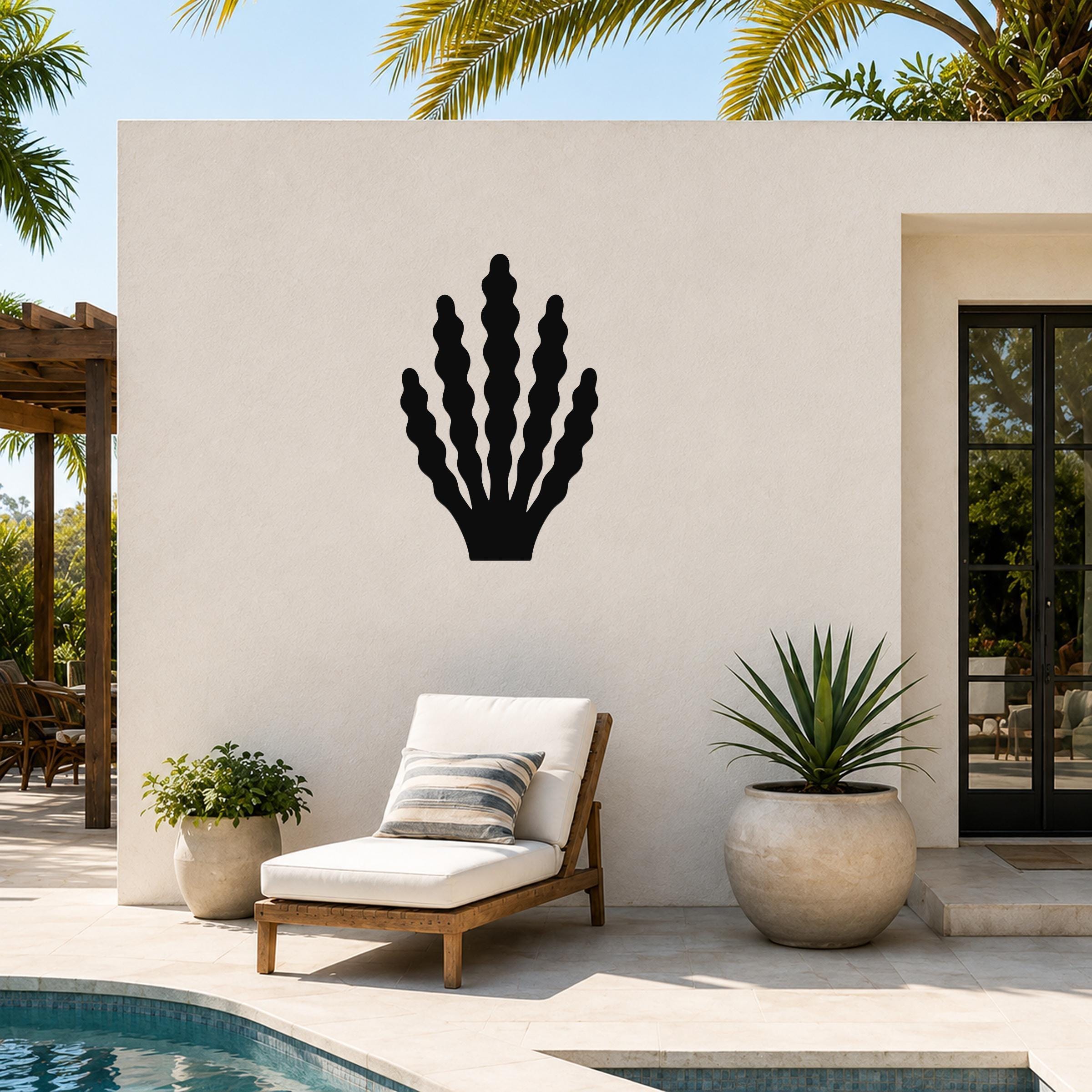 Black metal kelp wall art with wavy frond cutouts, mounted on an outdoor patio wall above a lounge chair near a pool.