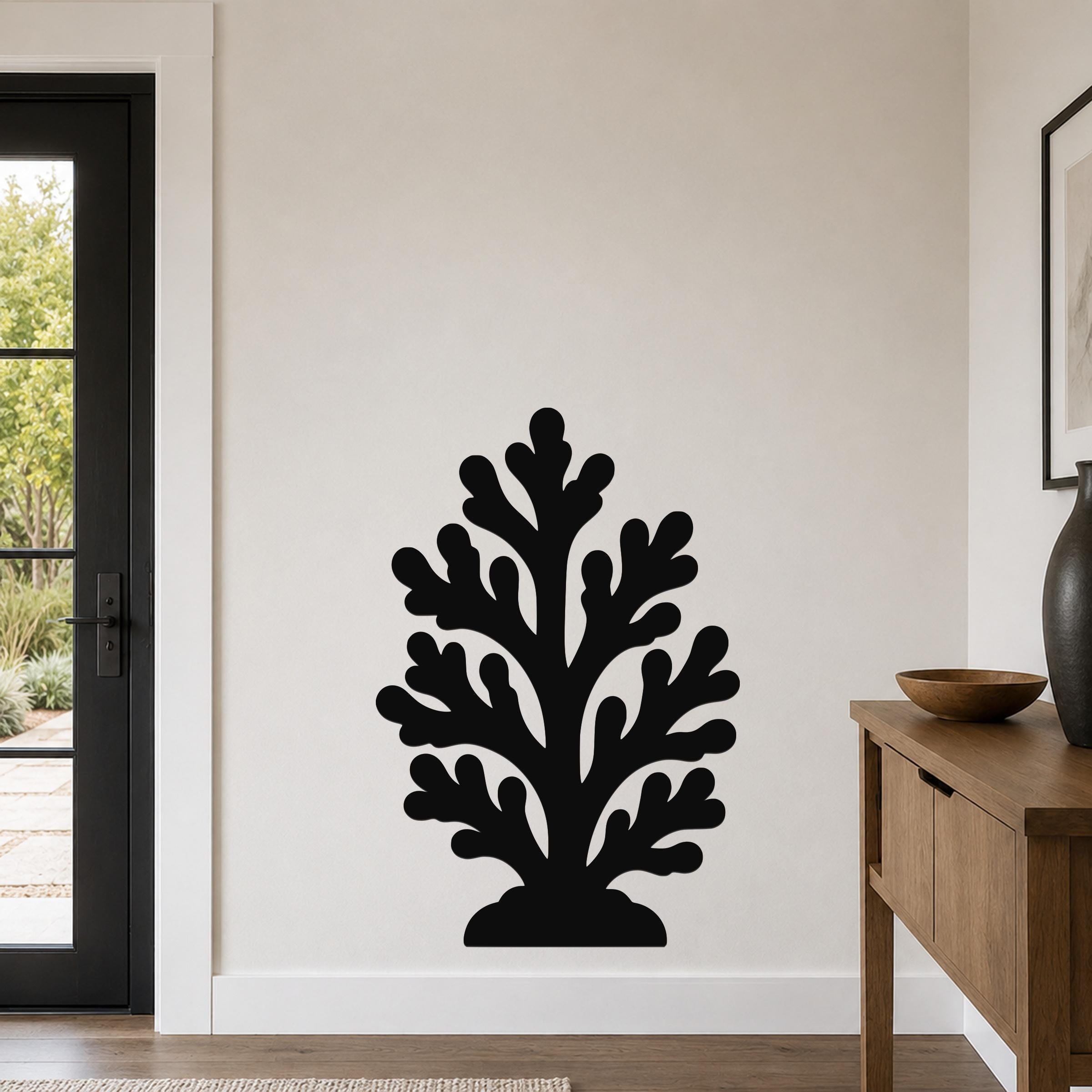 Black metal coral wall art with leafy cutout branches, mounted on a living room wall above a wooden console table.