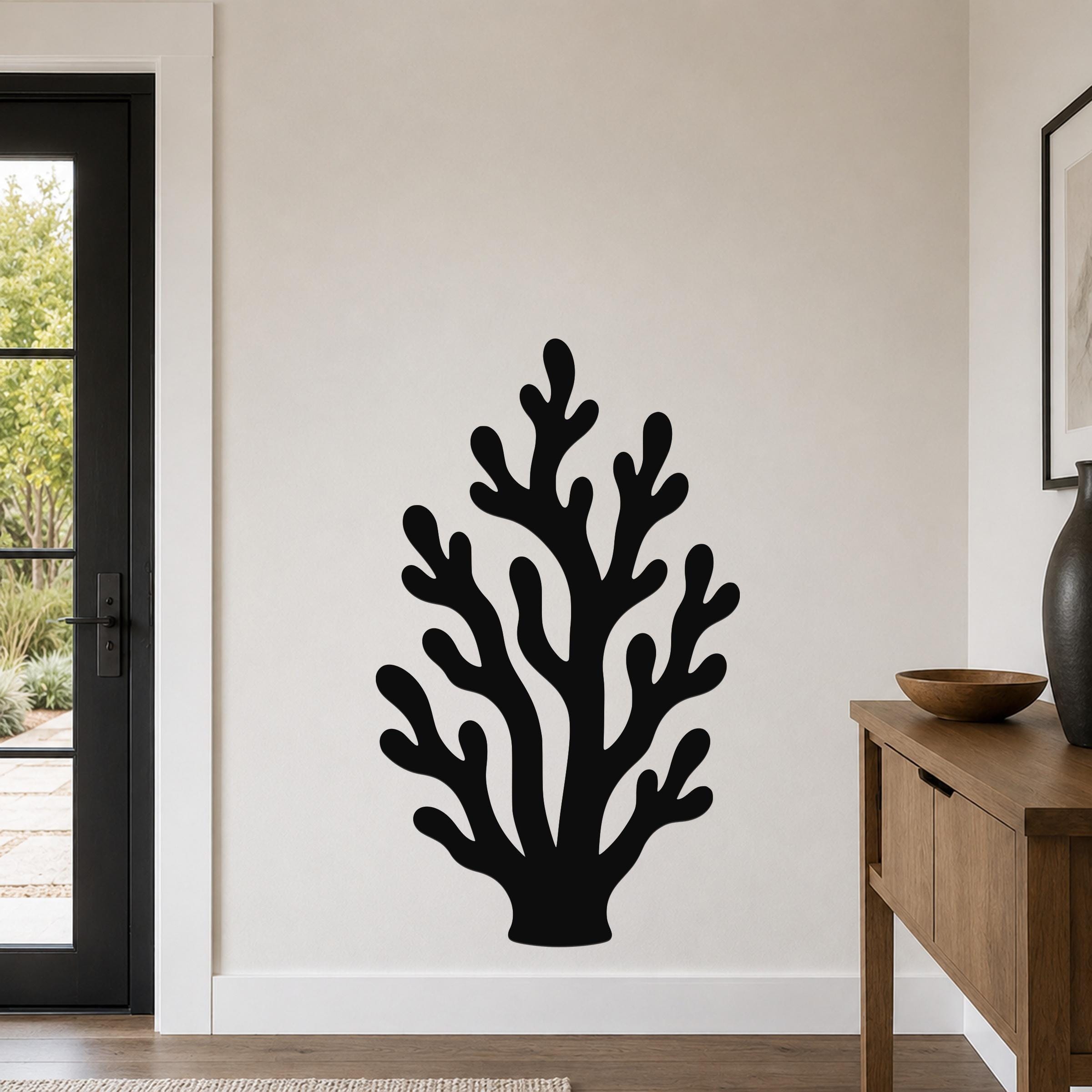 Black metal coral wall art with branching cutouts, mounted on a white wall in a living room near a door and console table.