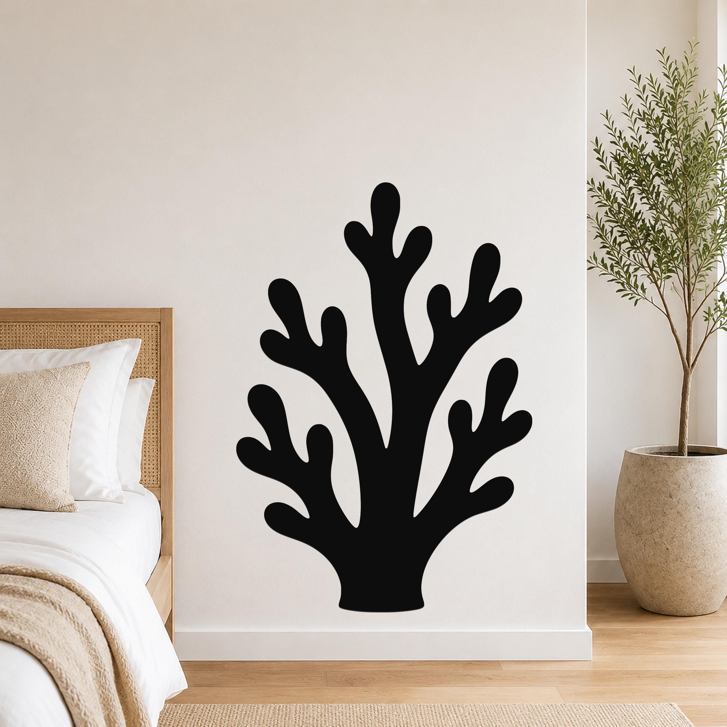 Black metal wall art in a branching coral silhouette, mounted on a white bedroom wall above a bed with a woven headboard.