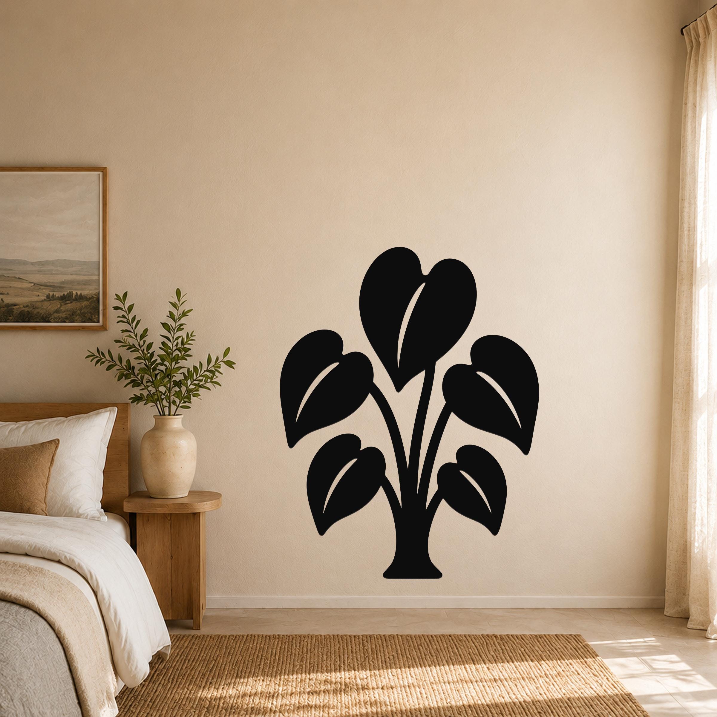 Black metal wall art in the shape of an elephant ear plant with large leaf cutouts, mounted on a beige bedroom wall above a woven rug.