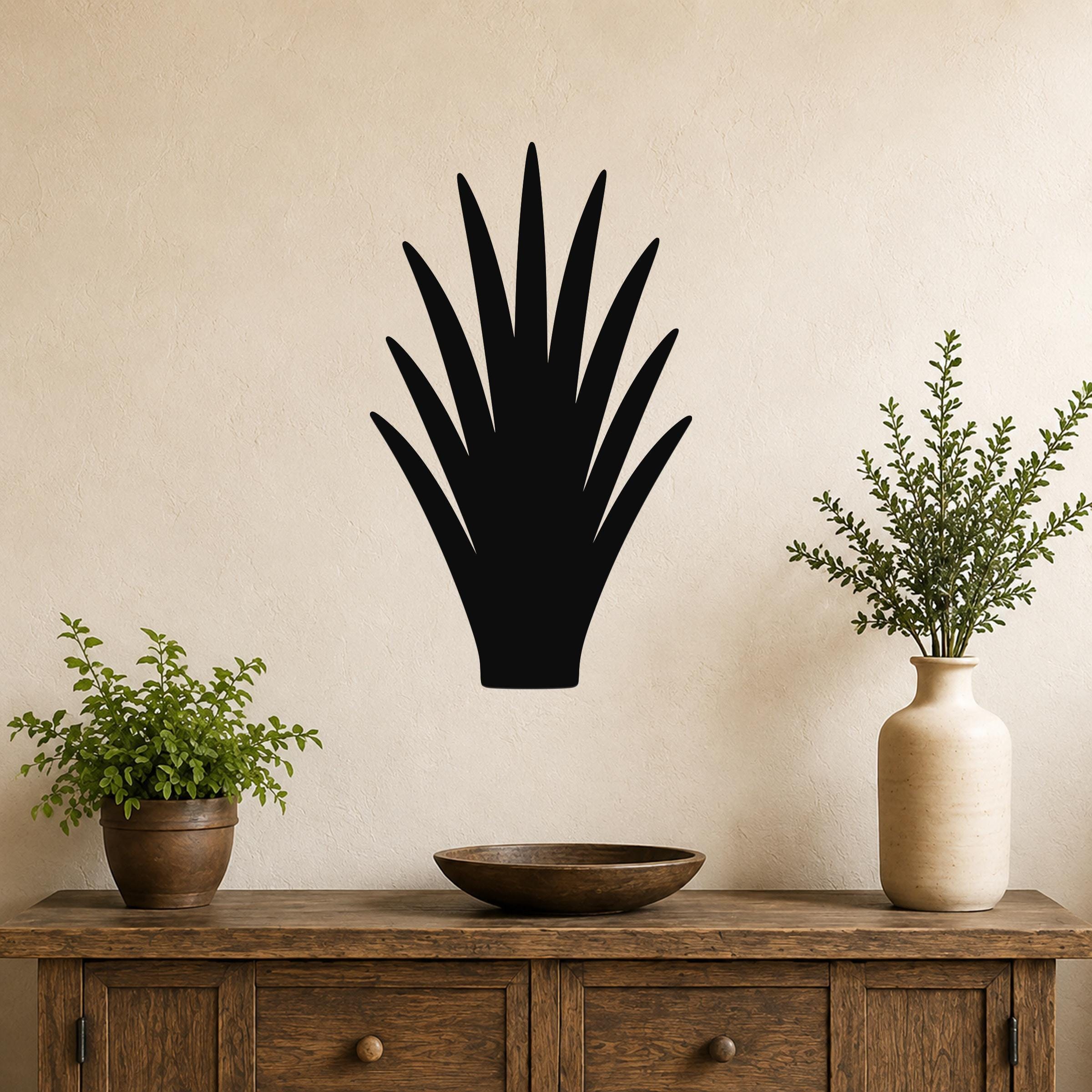 Black metal wall art in the silhouette of a spiky desert plant, mounted on a beige wall above a wooden console table with potted greenery.