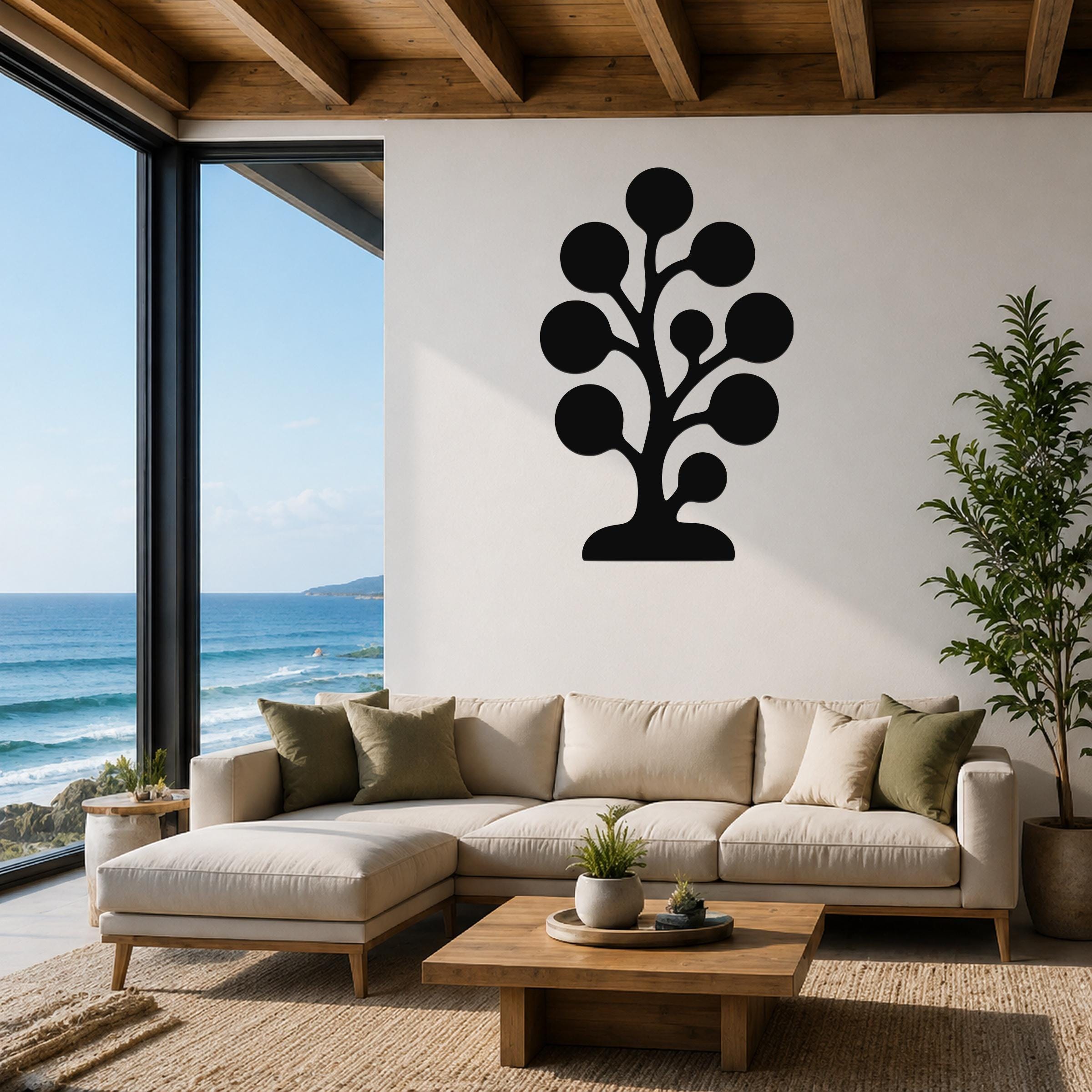 Black metal wall art in a kelp or seaweed silhouette design, mounted on a white living room wall above a beige sectional sofa with ocean views through large windows.
