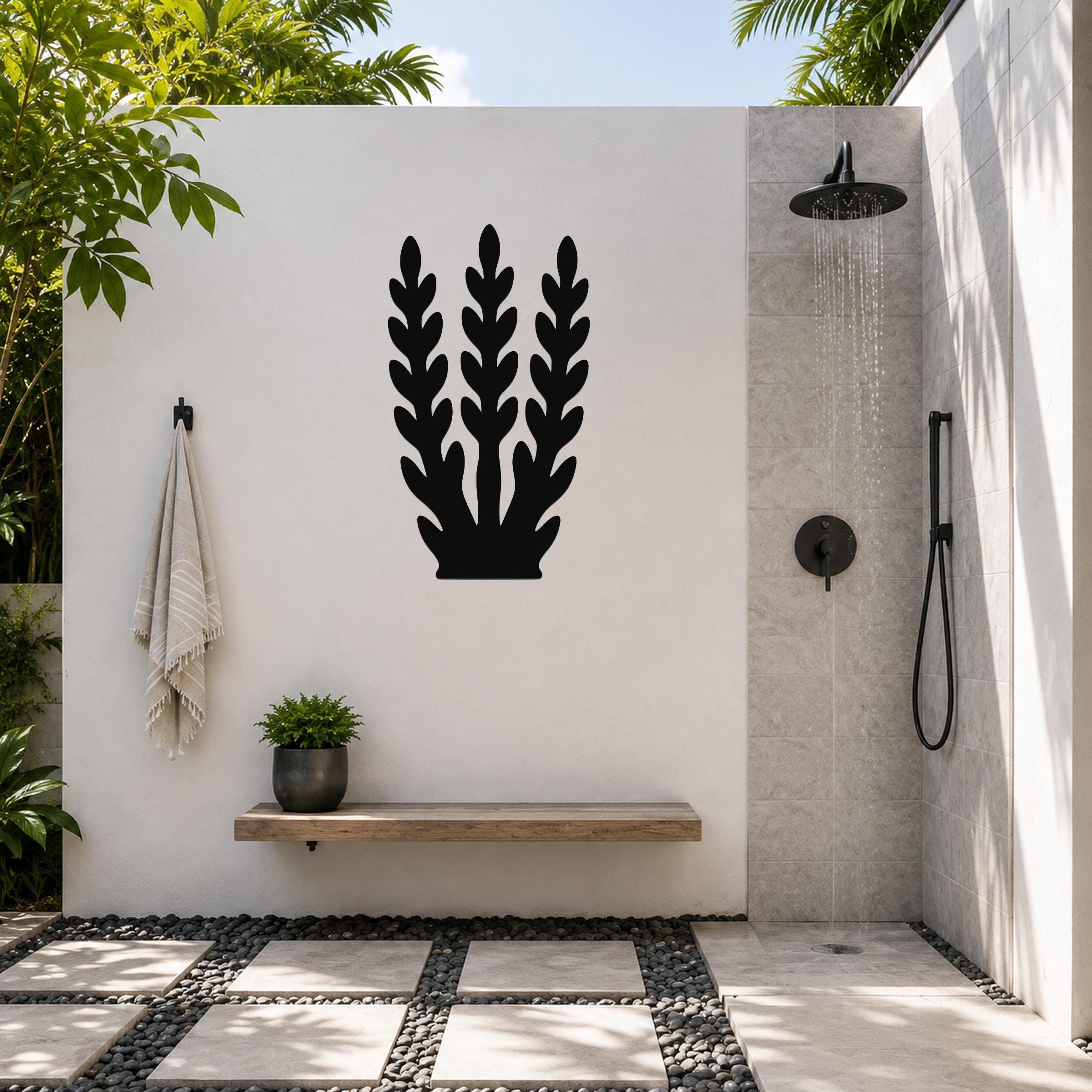 Black metal wall art in a kelp or seaweed silhouette design, mounted on a white outdoor wall above a wooden bench in a modern shower area.