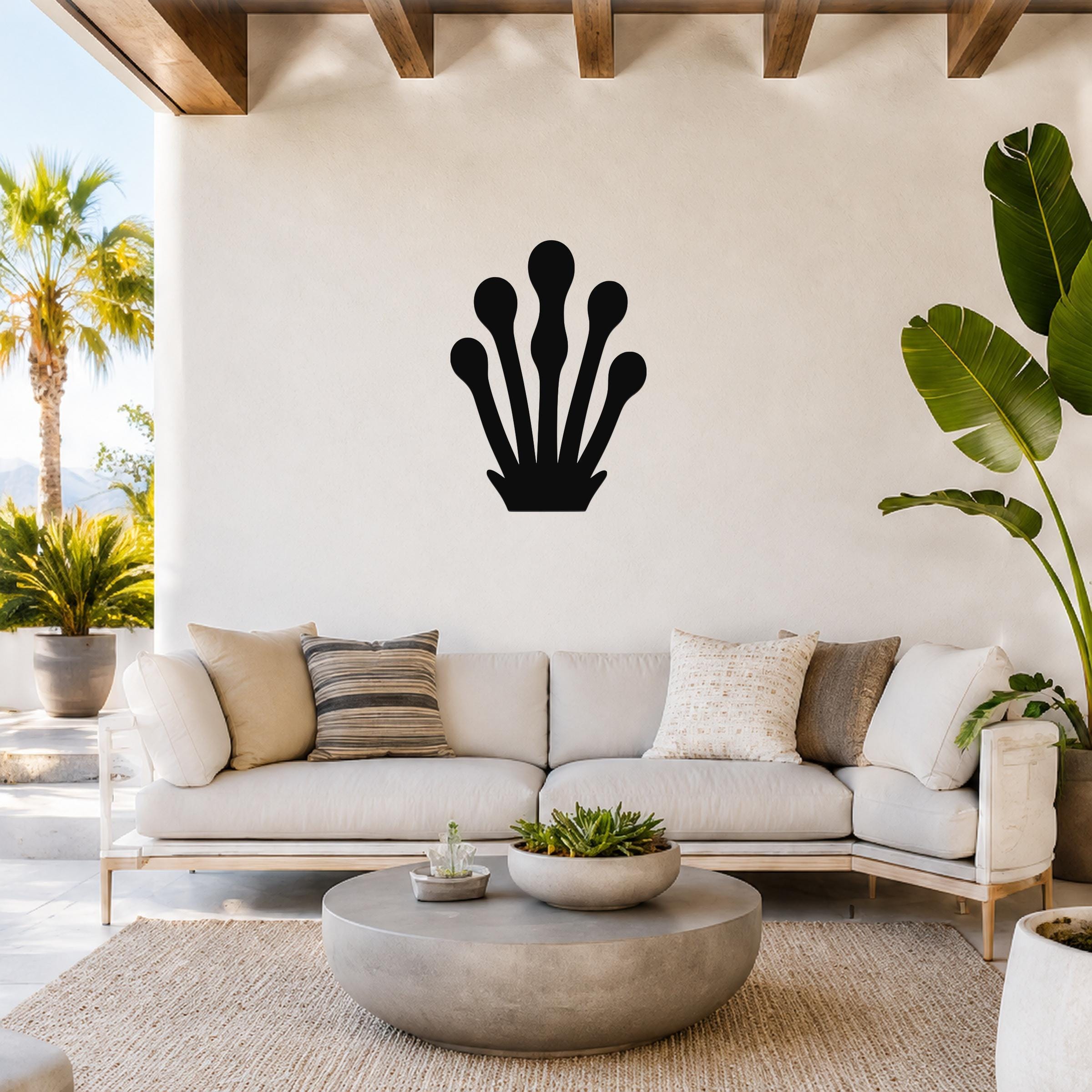 Black metal kelp wall art with five elongated frond cutouts, mounted on a white wall above a light-colored sofa in a bright outdoor living space.