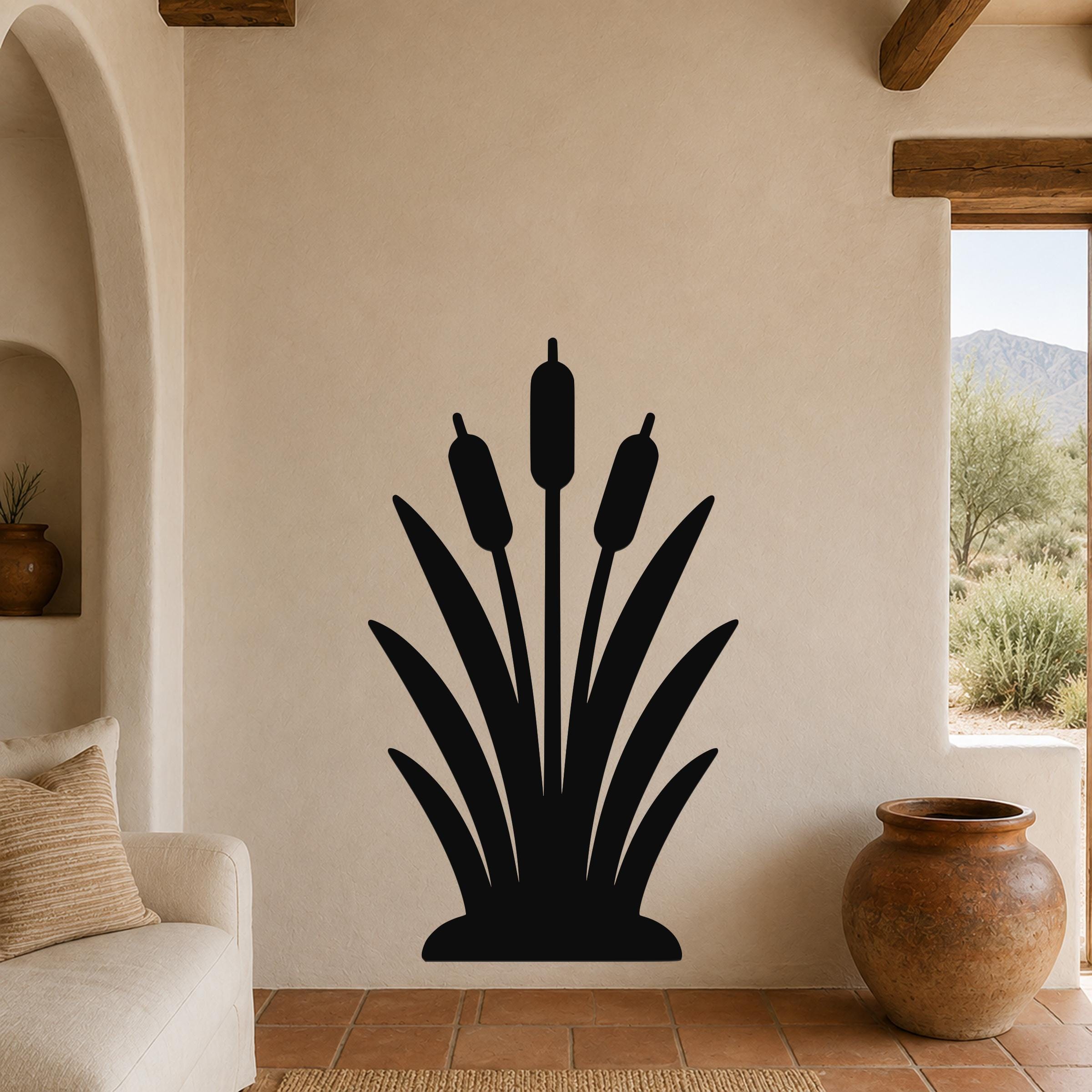 Black metal cattail wall art silhouette with three seed heads and long leaves, mounted on a beige living room wall above a sofa.