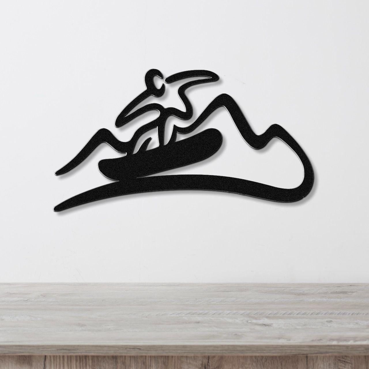 Black metal wall sculpture with a minimalist snowboarder silhouette and mountain cutout design, mounted on a white wall above a wooden counter.
