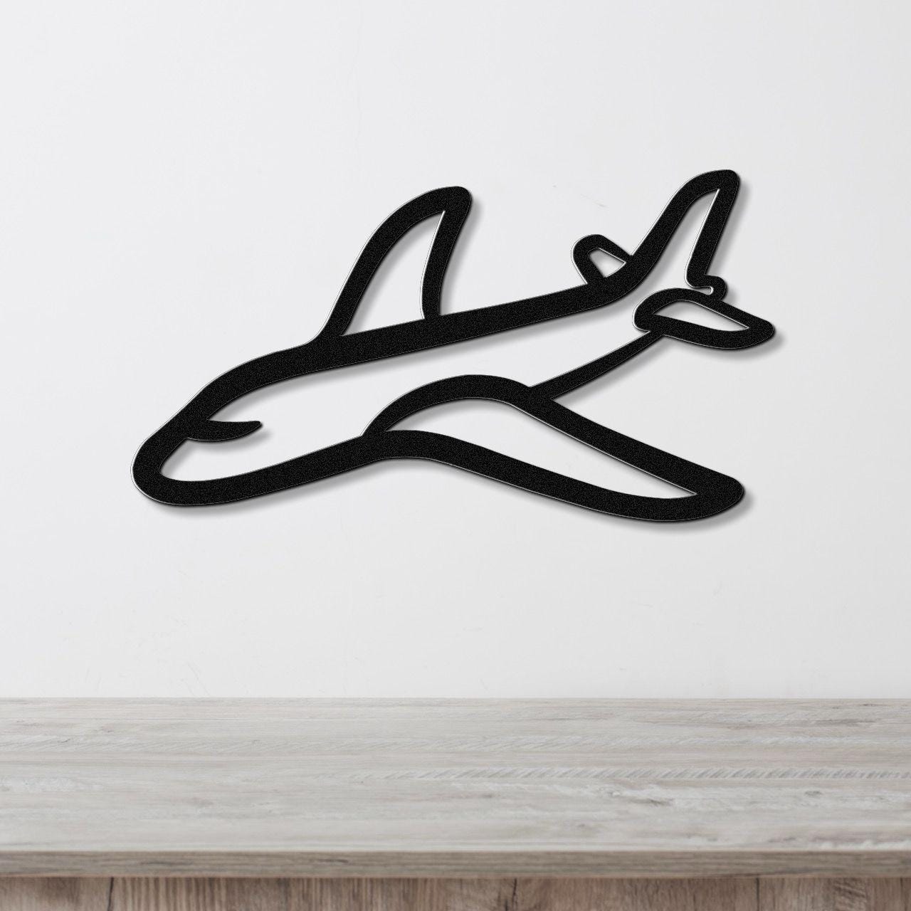 Black metal airplane wall art with a sleek silhouette design, mounted on a white wall above a light wood countertop.