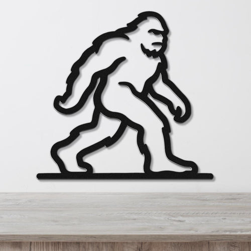 Black metal wall art silhouette of Bigfoot in a walking pose, mounted on a white wall above a wooden surface.