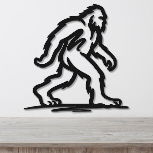Black metal wall art silhouette of a Bigfoot figure in a walking pose, mounted on a white wall above a wooden surface.