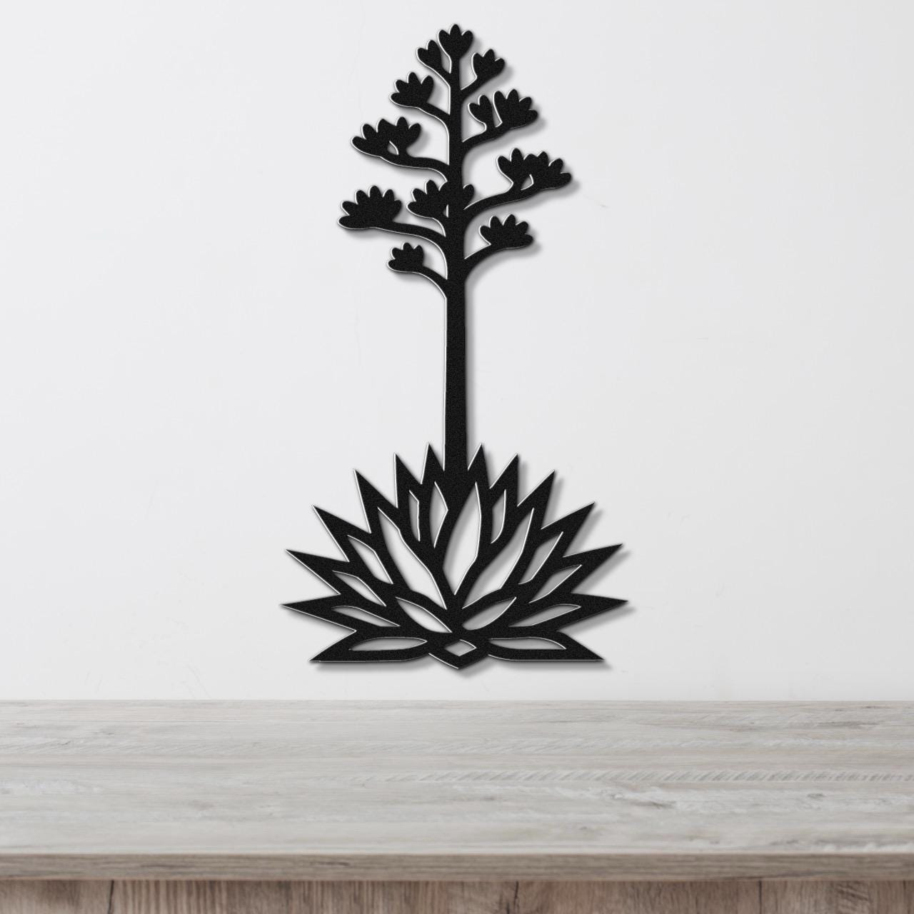 Black metal wall art cutout of a blooming agave plant with a tall stem and flower spikes, mounted on a white wall above a light wood surface.
