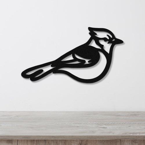 Black metal blue jay wall art silhouette with internal cutout details, mounted on a white wall above a light wood surface.