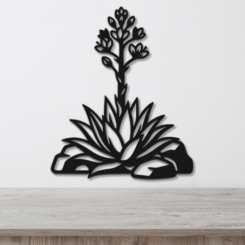 Black metal wall art in a cutout silhouette of a blooming agave plant with spiky leaves and flower stalk, mounted on a white wall above a wooden surface.