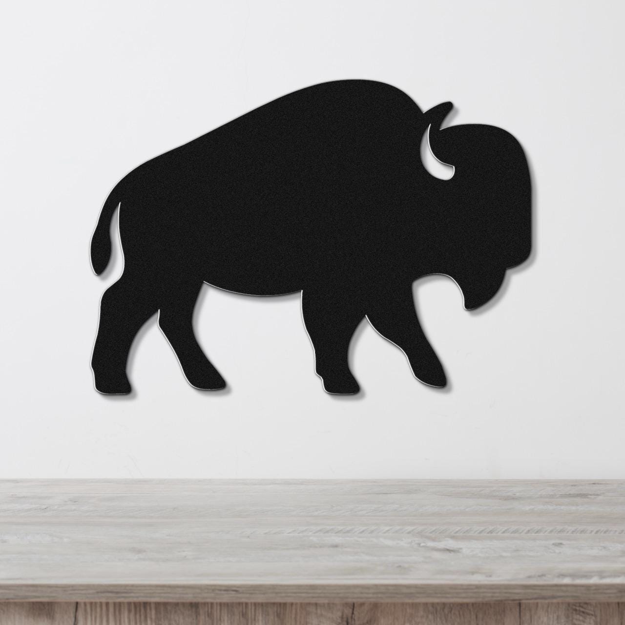 Black metal buffalo wall art silhouette with horn and tail cutouts, mounted on a white wall above a light wood counter.