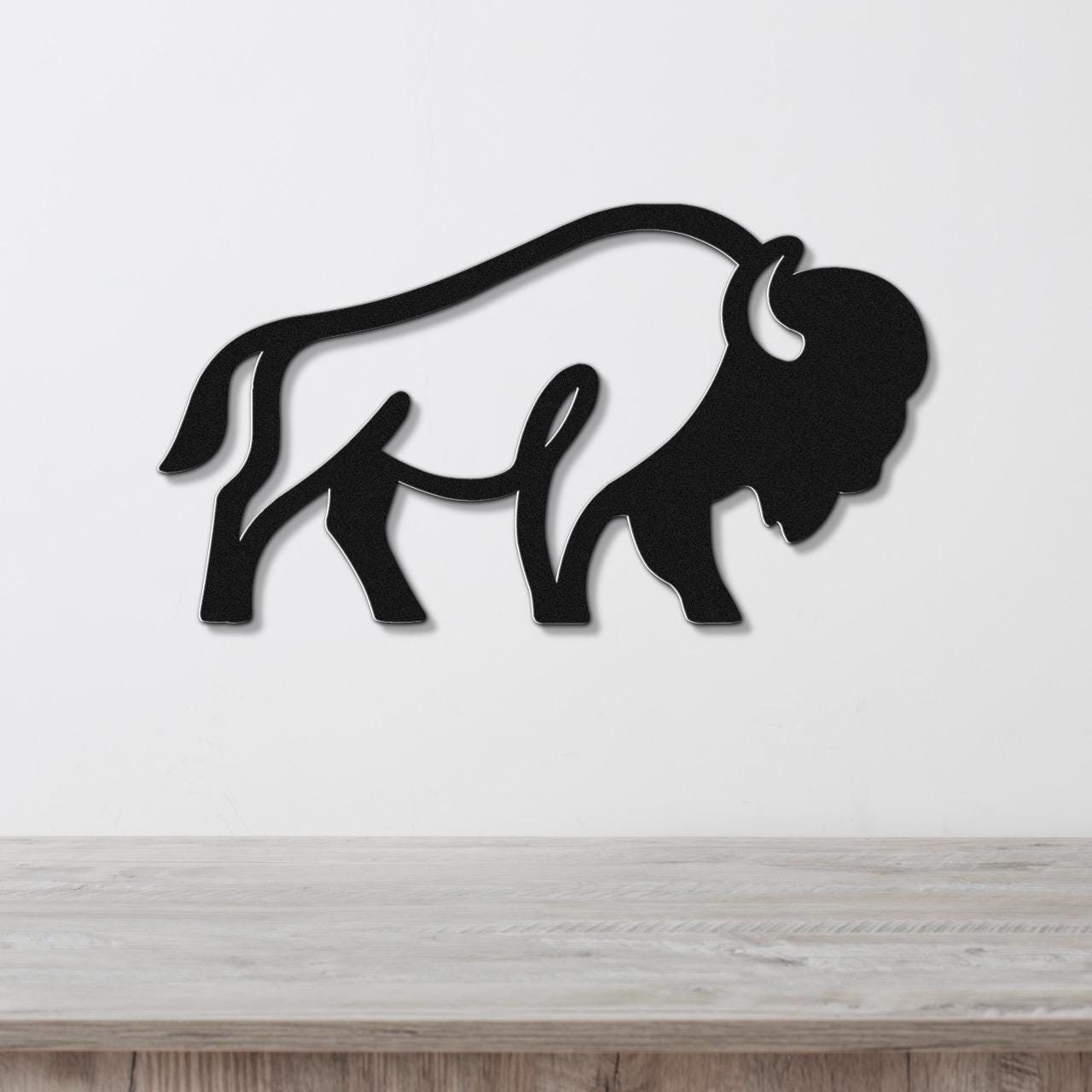 Black metal bison silhouette wall art with cutout horns and tail, mounted on a white wall above a light wood counter.