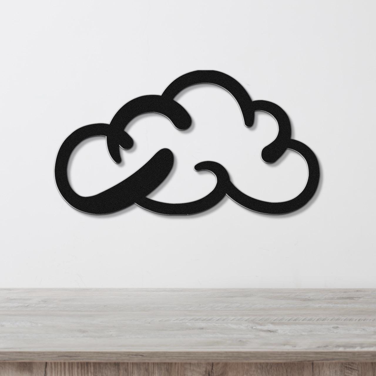 Black metal cloud-shaped wall art with internal cutout details, mounted on a white wall above a light wood surface.