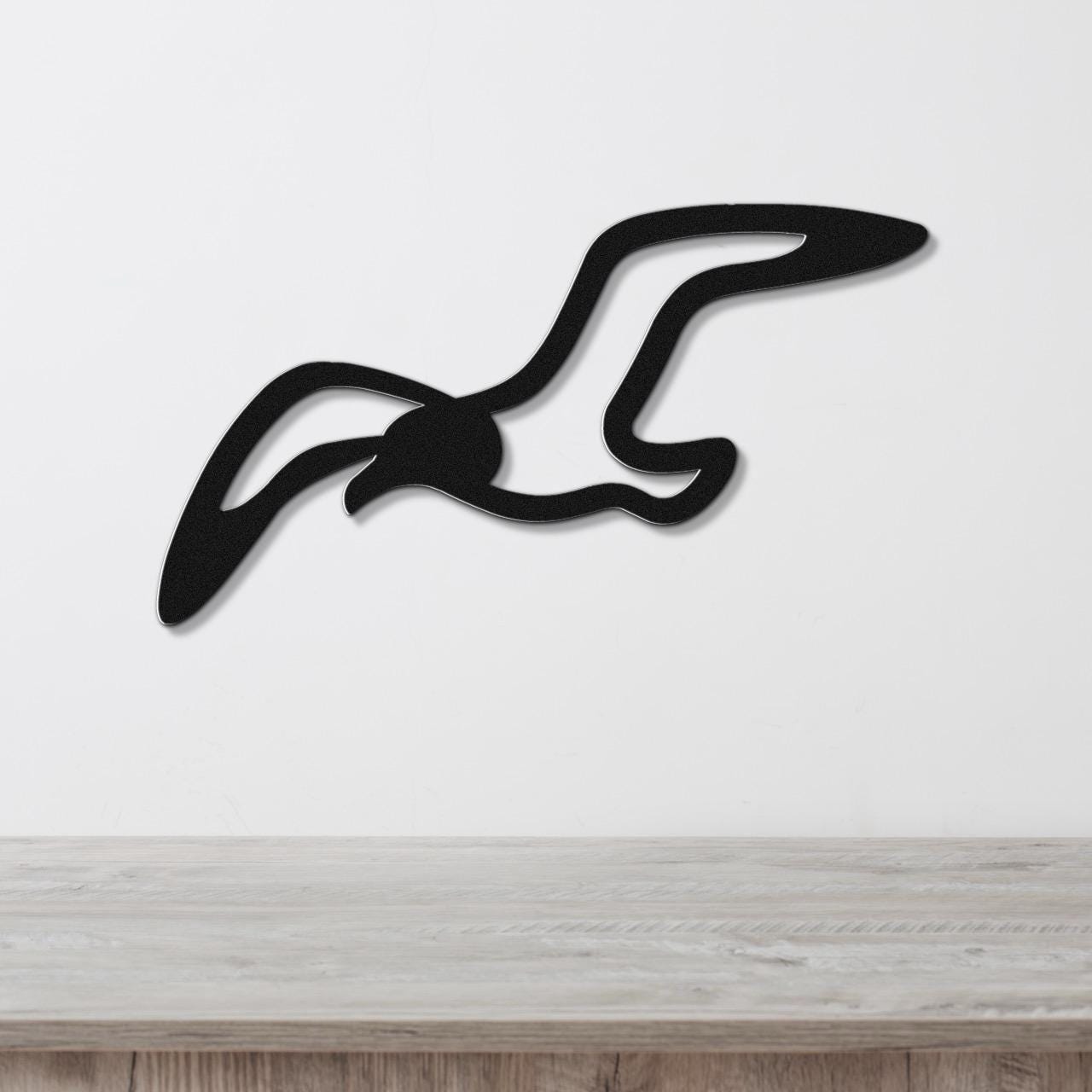 Black metal seagull wall art with a cutout silhouette design, mounted on a white wall above a light wood surface.