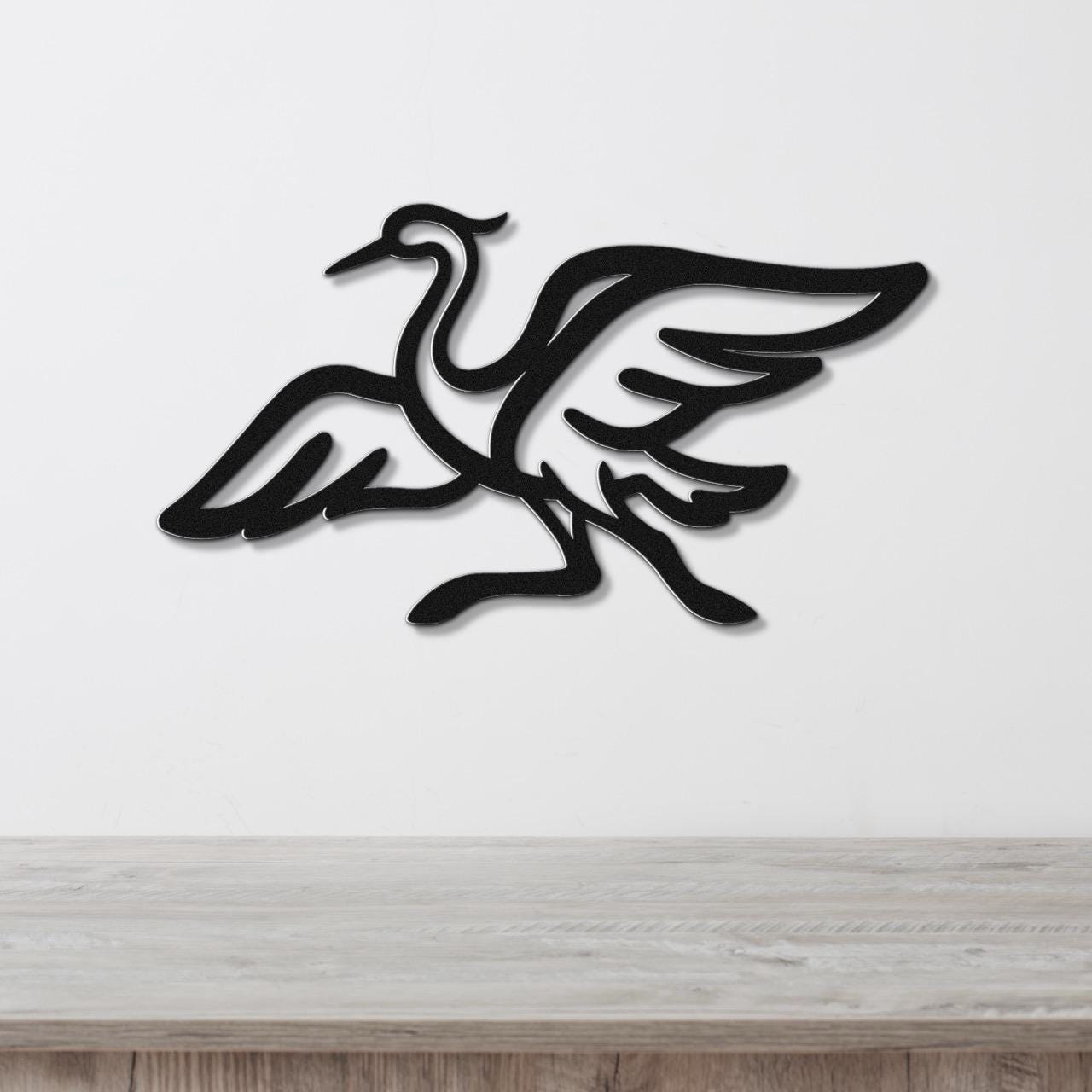Black metal crane wall art with wing and leg cutouts, mounted on a white wall above a light wood surface.