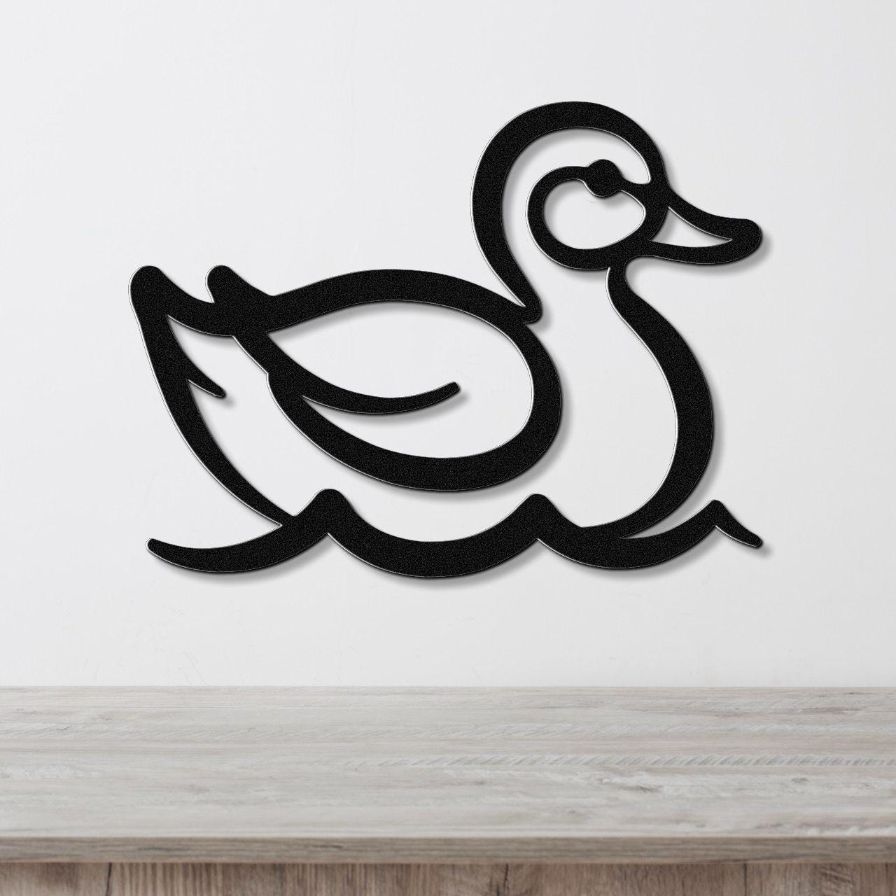 Black metal duck wall art with a silhouette design, mounted on a white wall above a light wood surface.